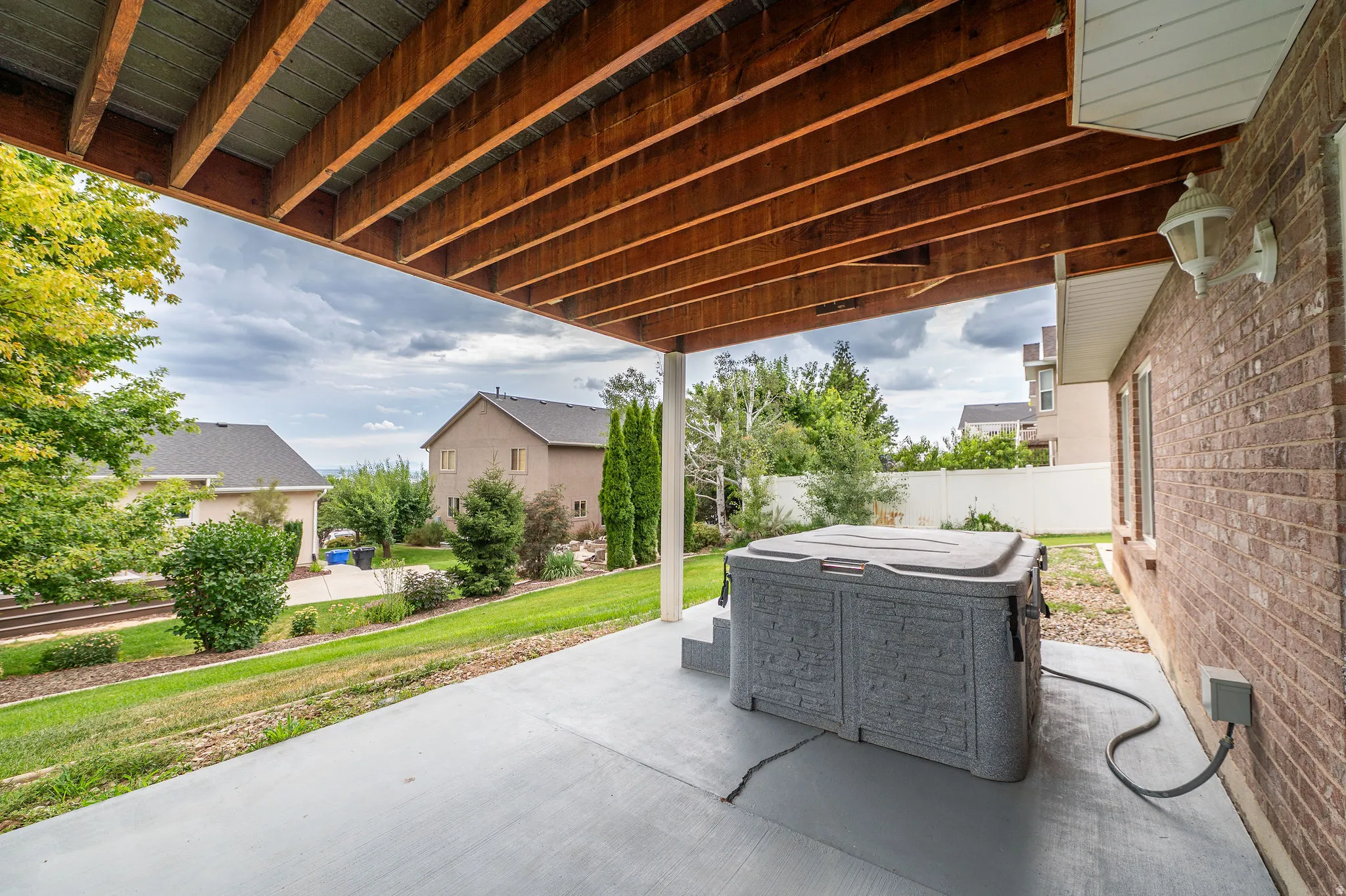 Covered patio featuring a hot tub with built-in steps, a brick exterior wall, and a wood-beamed ceiling
