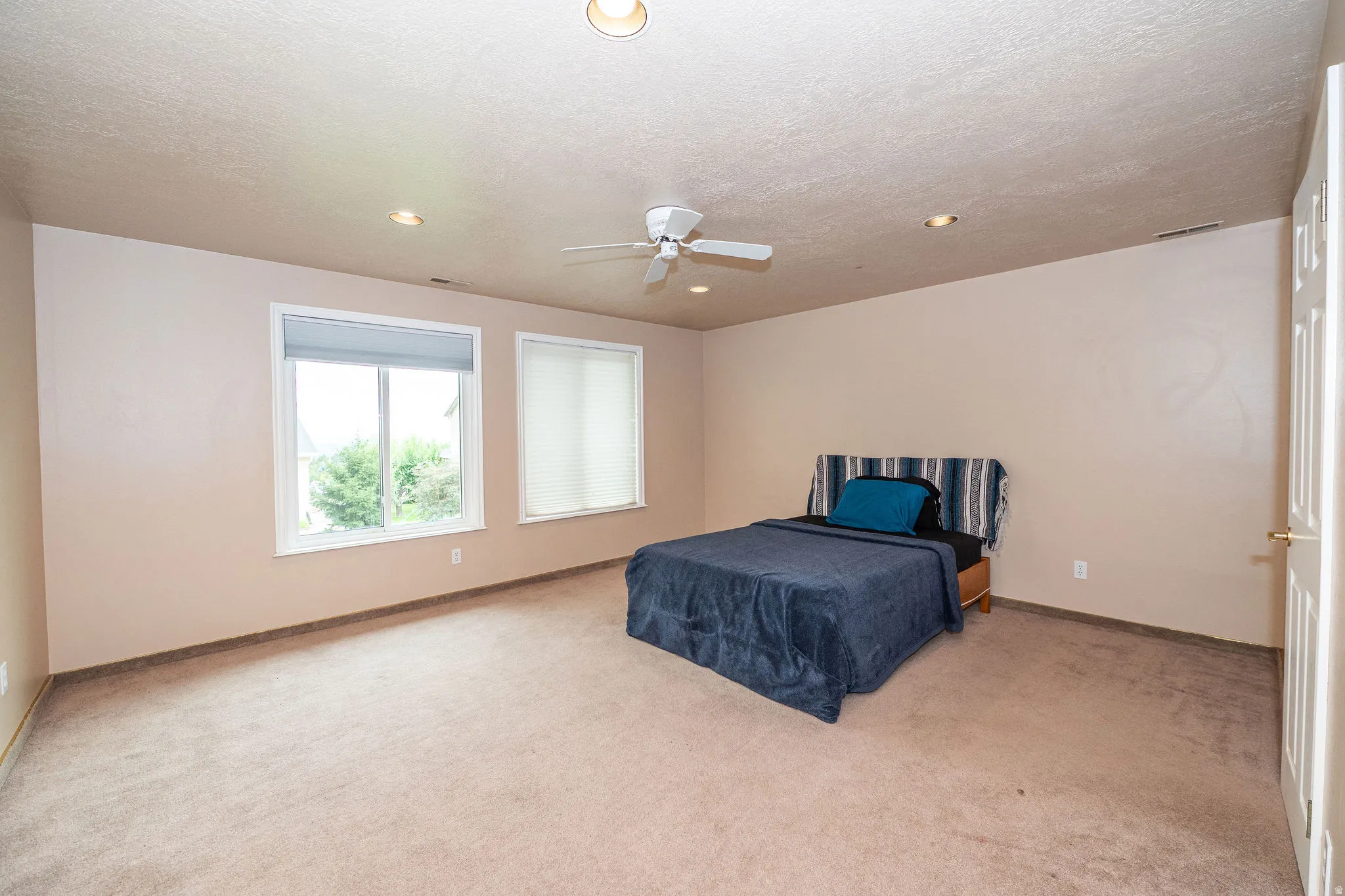 Spacious room featuring neutral carpeting, two windows with blinds, recessed lighting, and a ceiling fan