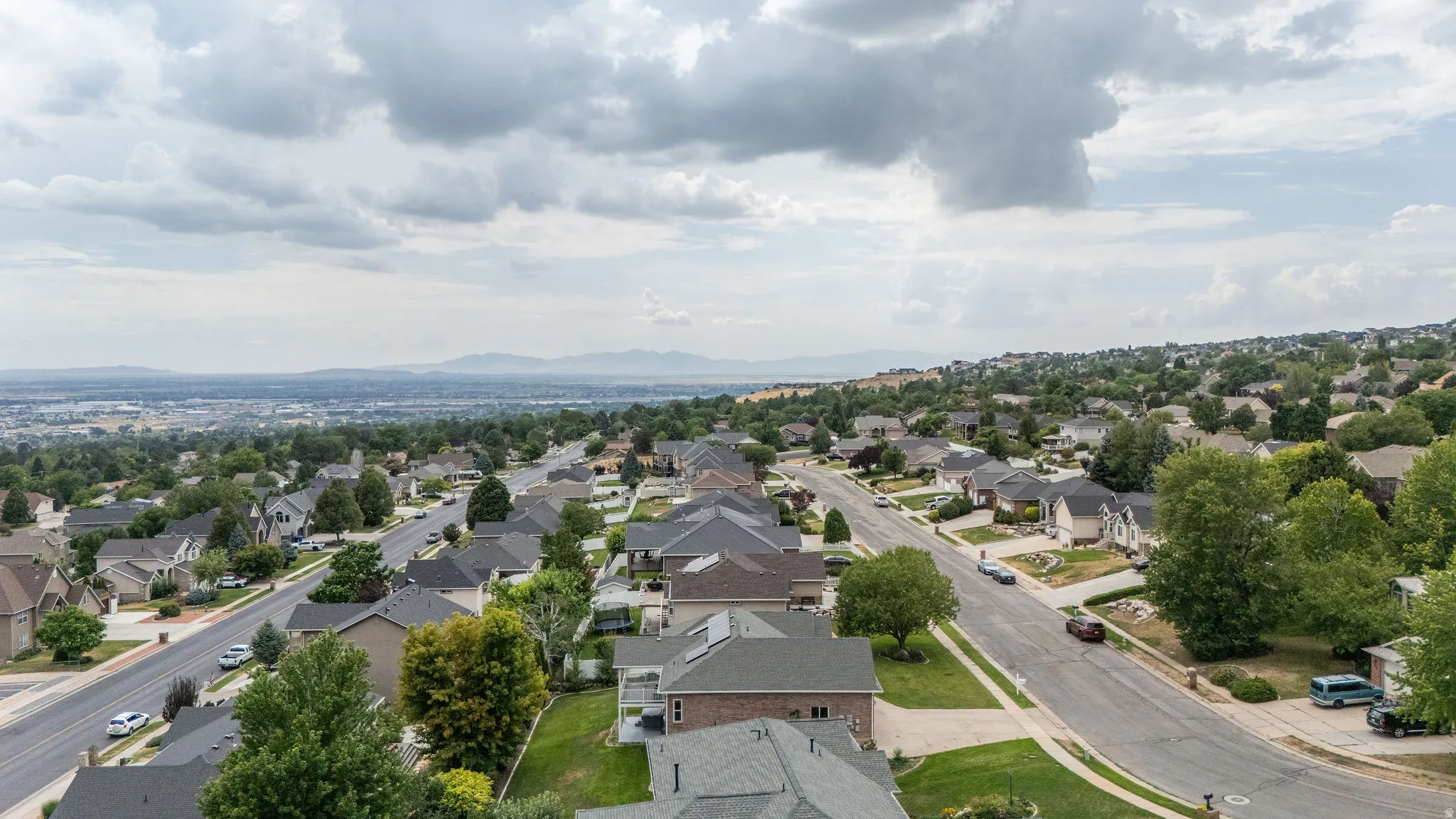 Expansive residential neighborhood featuring paved streets, mature trees, and distant mountain ranges
