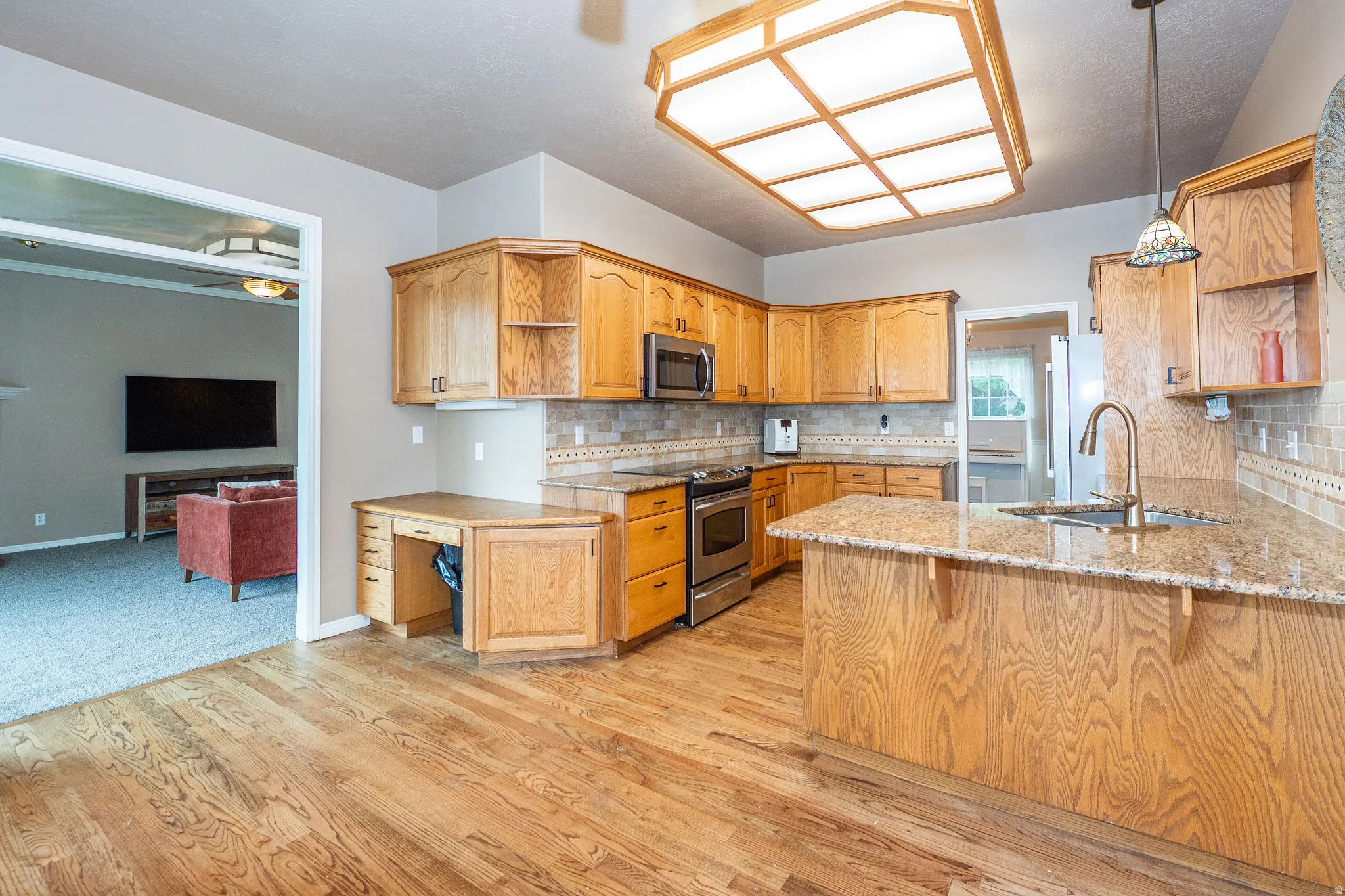 Kitchen featuring wood-finish flooring, light wood cabinetry, stainless steel appliances, granite countertops, and a tiled backsplash