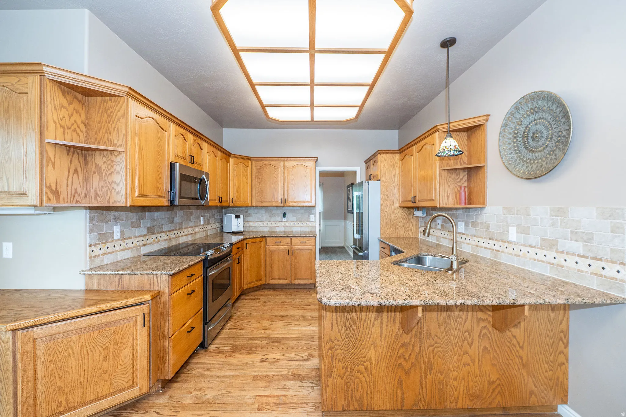 Kitchen featuring ample wood cabinetry, granite countertops, stainless steel appliances, a tiled backsplash, and wood-finish flooring