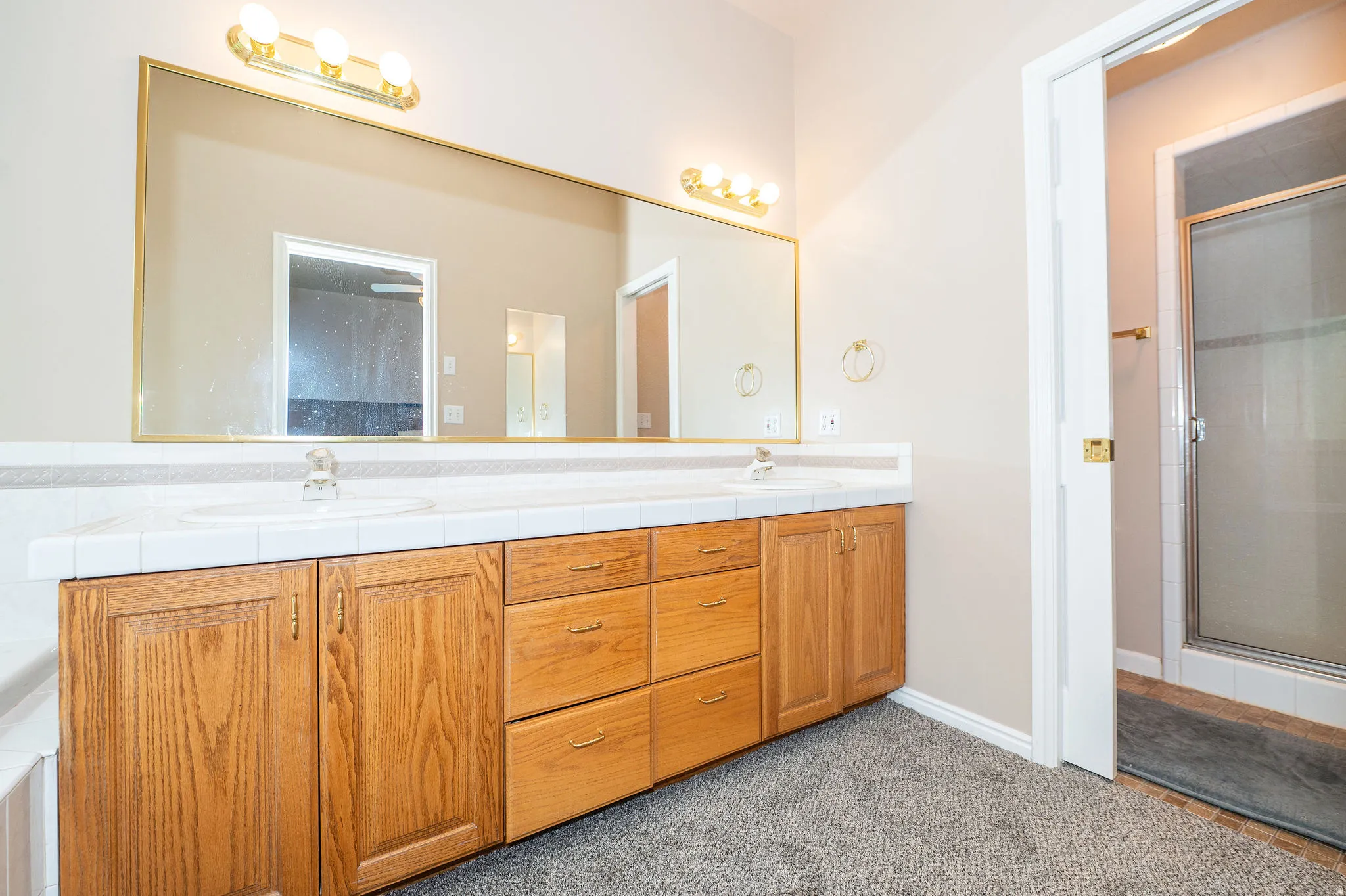 Dual vanity with wood-finish cabinetry, tile countertop, and integrated sinks