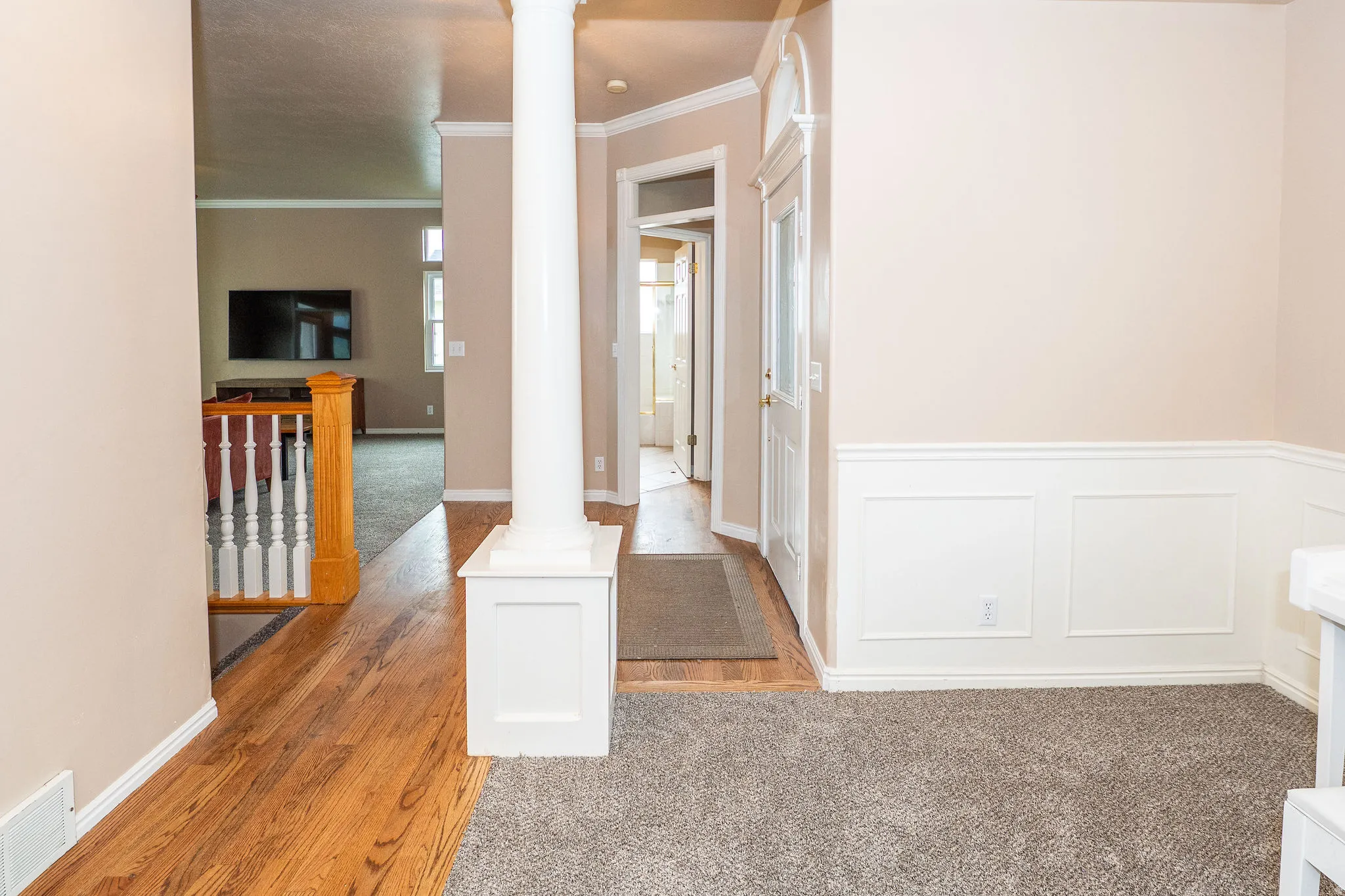 Entryway featuring a decorative column, wainscoting, wood-finish flooring, and a glass-paneled door with an arched transom