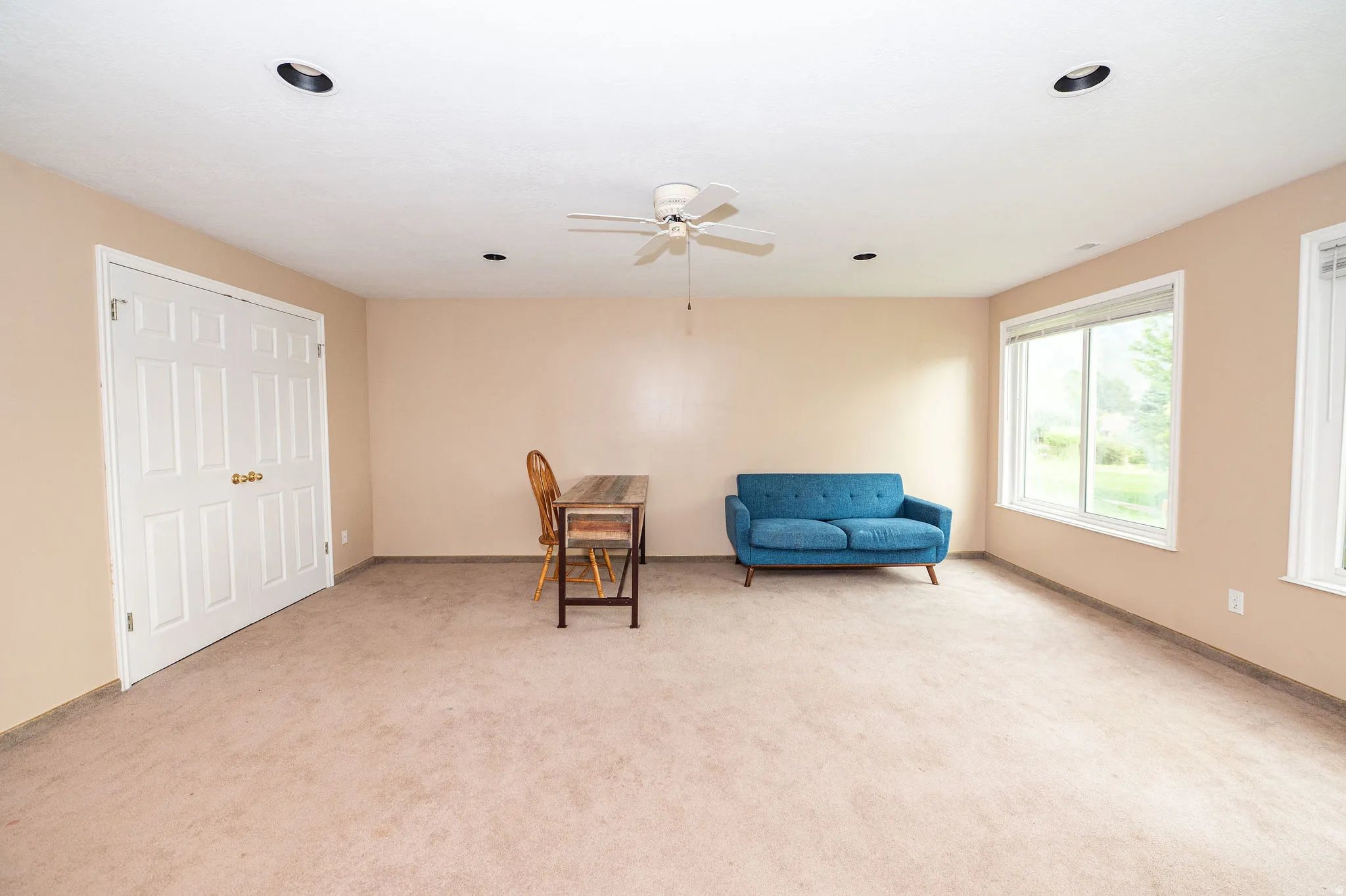 Spacious room featuring neutral carpeting, a ceiling fan, recessed lighting, and large windows with white trim