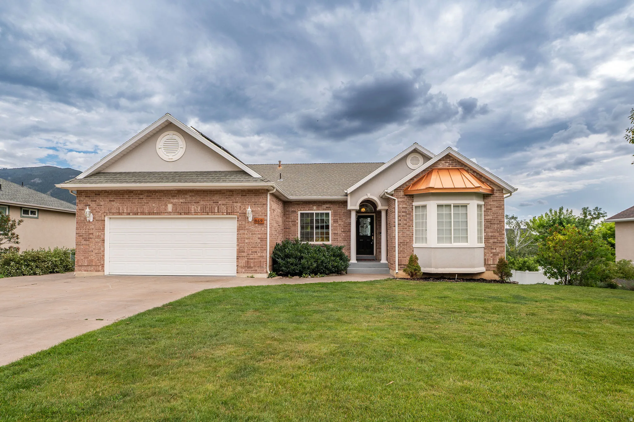 Brick and stucco exterior featuring a two-car garage, bay window with a copper-tone roof, and a covered entry
