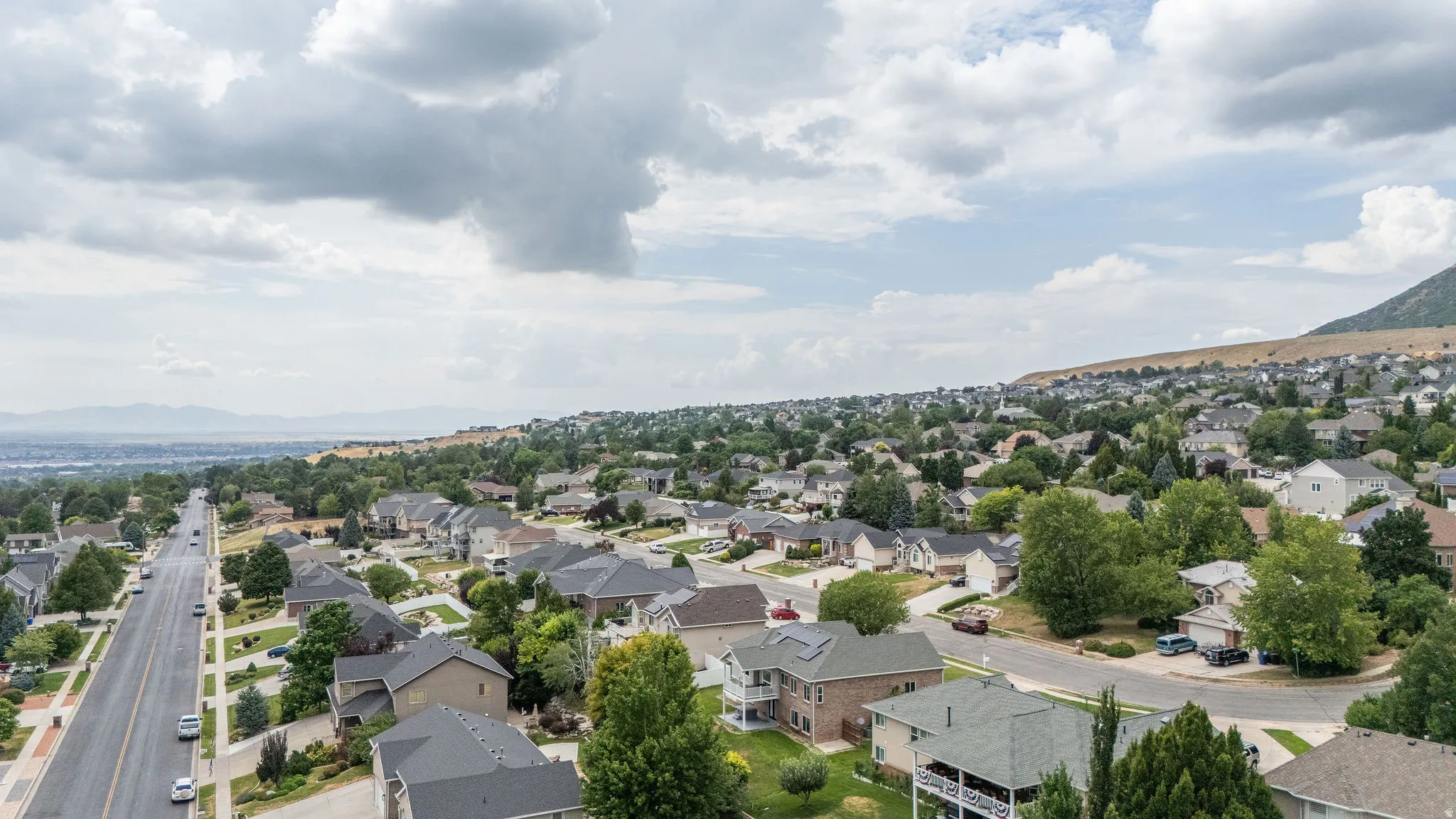 Expansive neighborhood situated on a hillside, featuring mature trees, paved streets, and distant mountain ranges