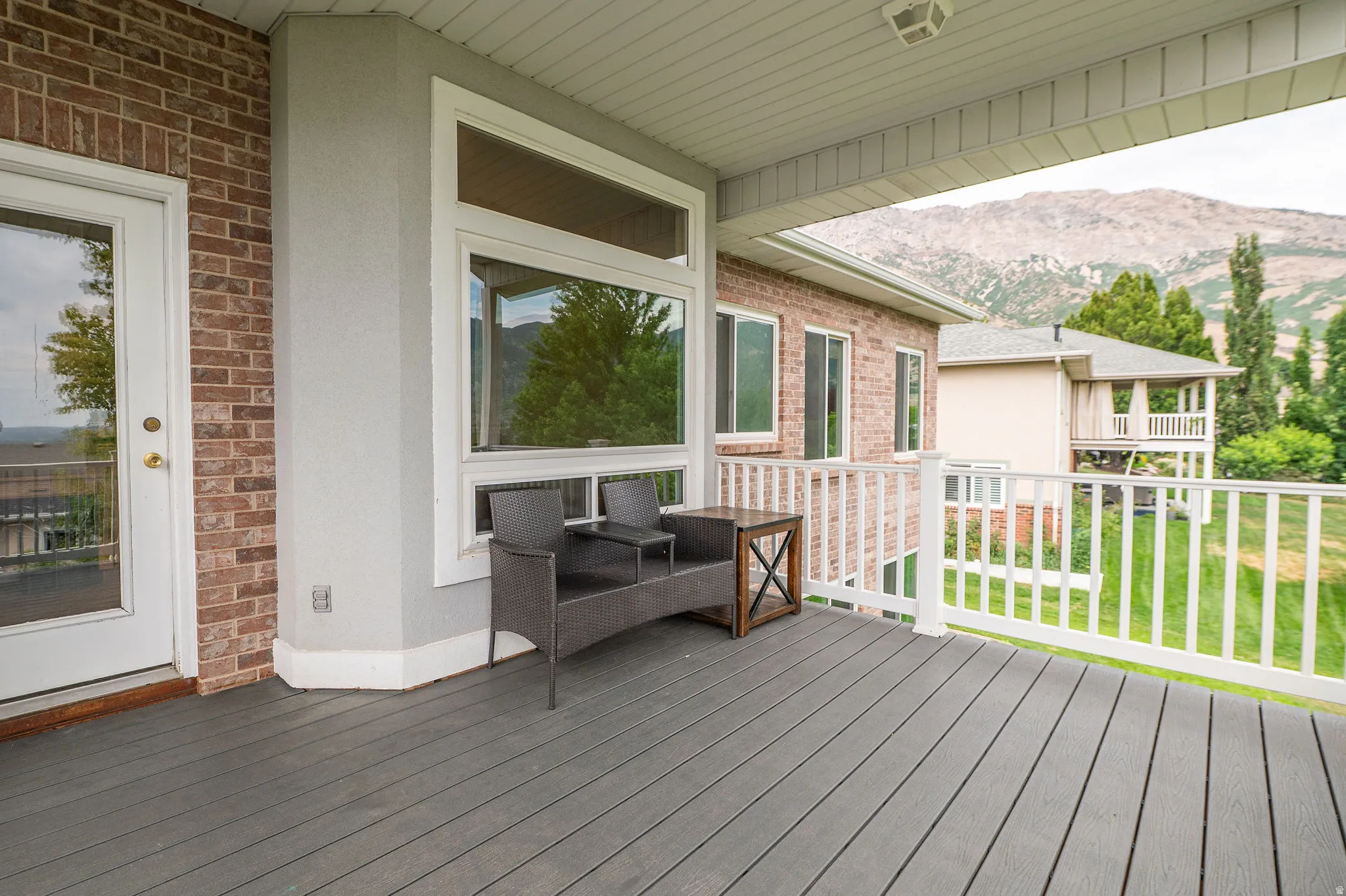 Covered outdoor patio featuring composite decking, white railing, and a brick exterior