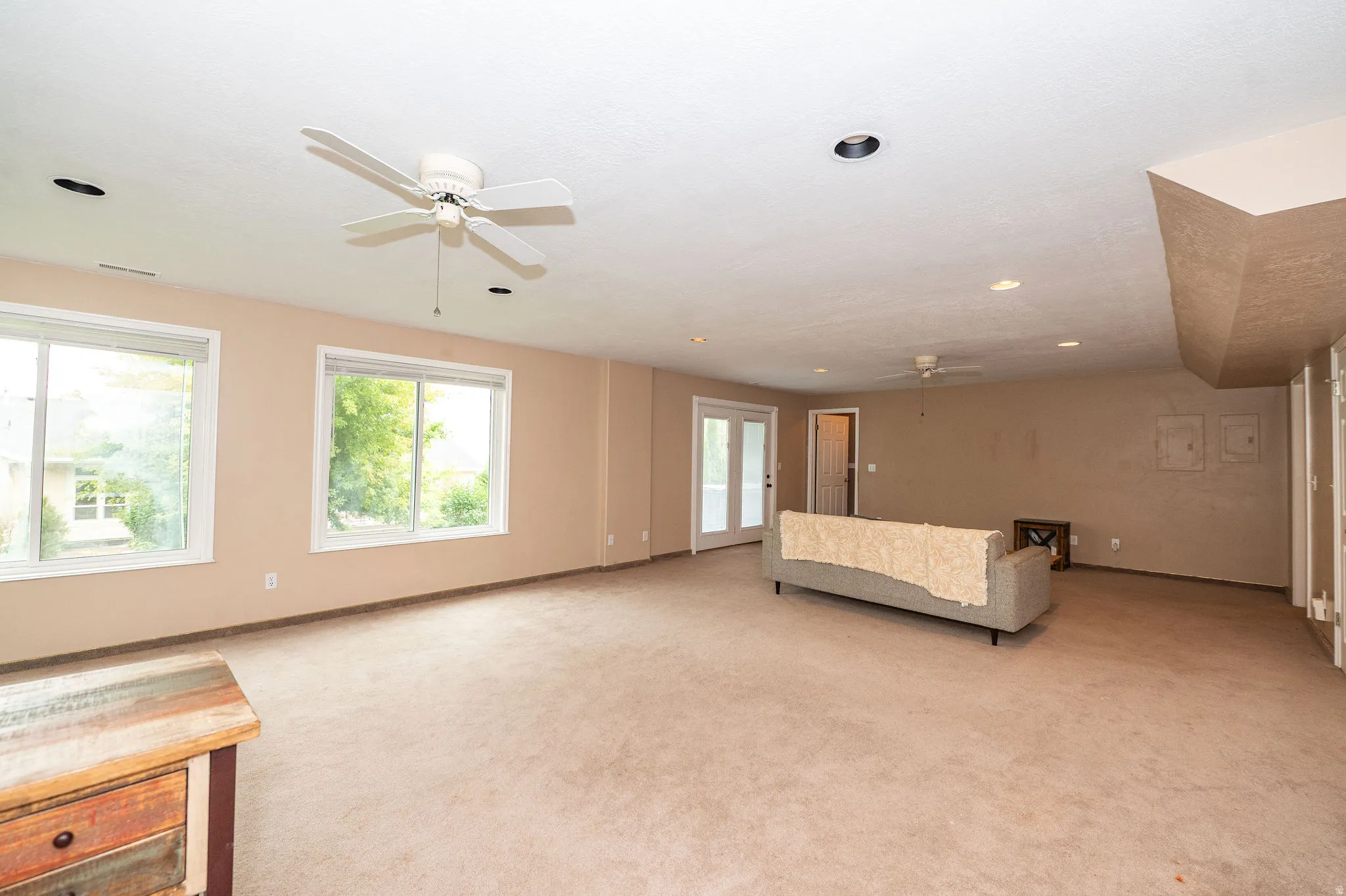 Spacious lower-level room featuring two large windows, double French doors, recessed lighting, and two ceiling fans