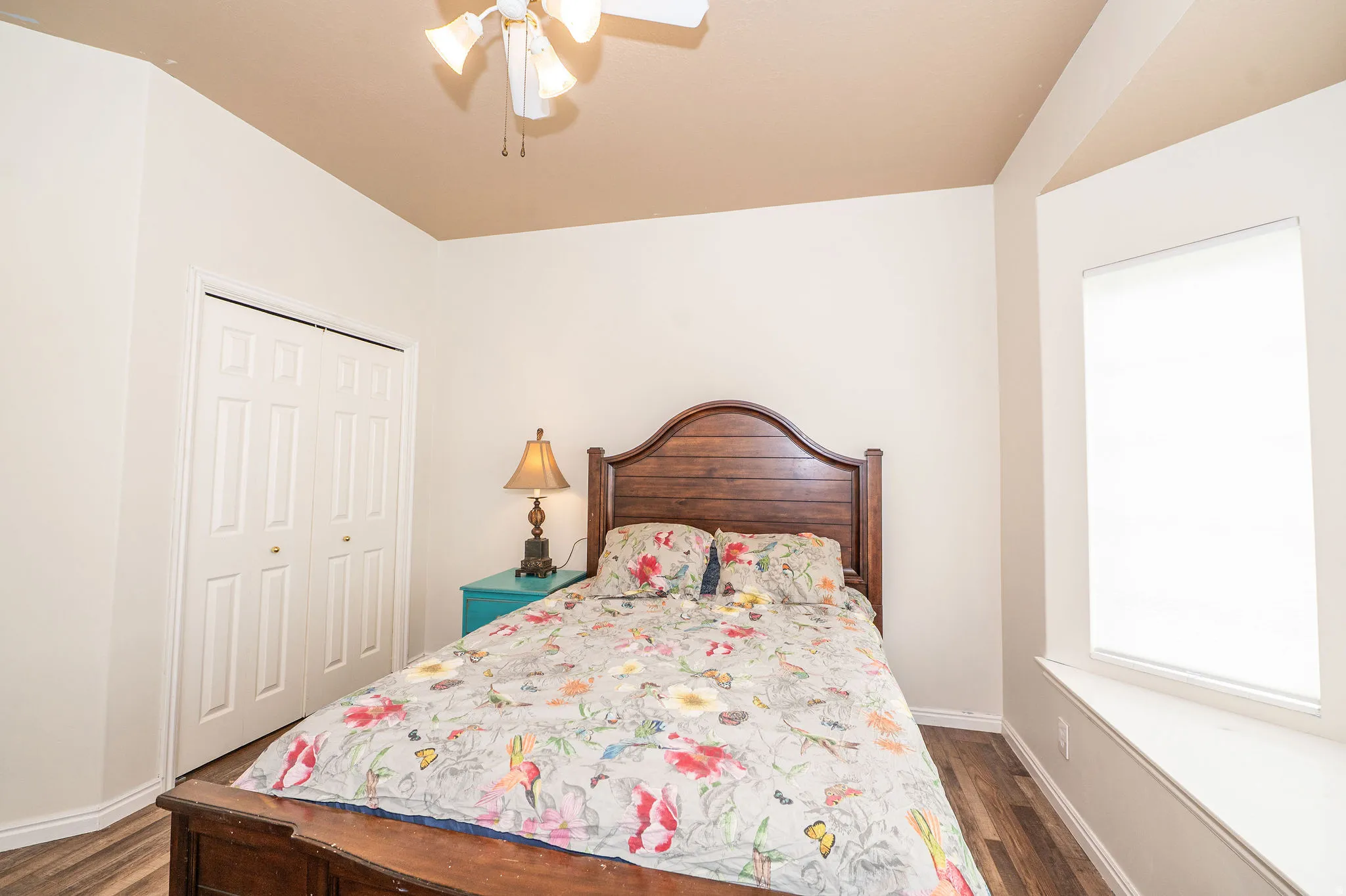 Bedroom featuring wood-finish flooring, a ceiling fan with integrated lighting, a bay window with a built-in window seat, and bi-fold closet doors