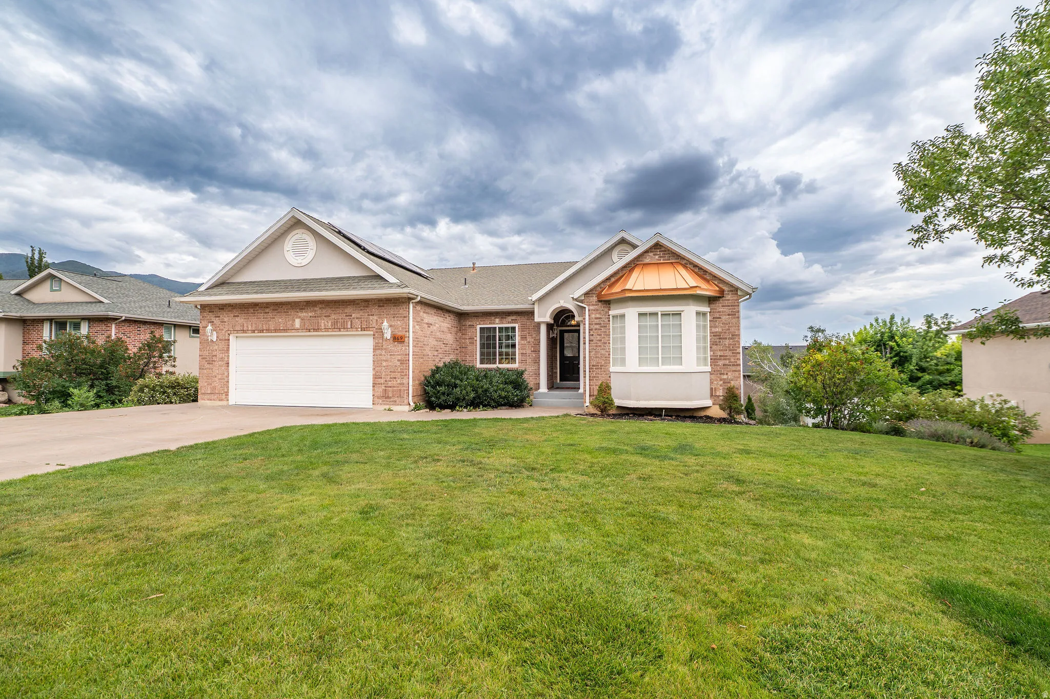 Brick exterior with a prominent front-facing garage, bay window featuring a copper-toned awning, and a gabled entry