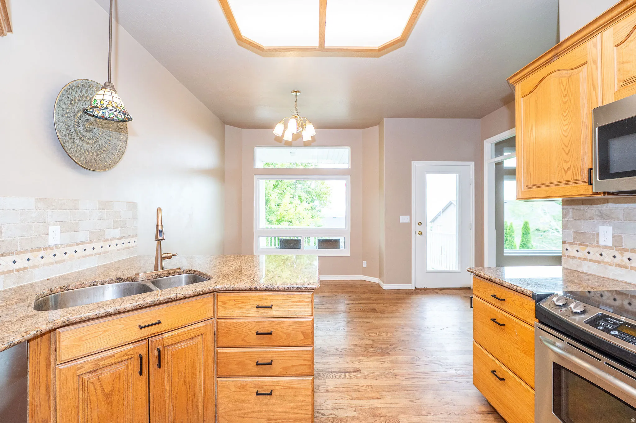 Kitchen featuring wood-finish flooring, light wood cabinetry, stone countertops, and a tiled backsplash