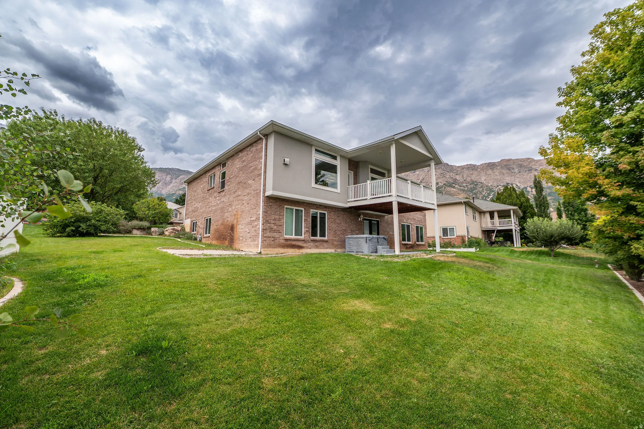 Expansive sloped lawn with mature trees and a brick and stucco exterior