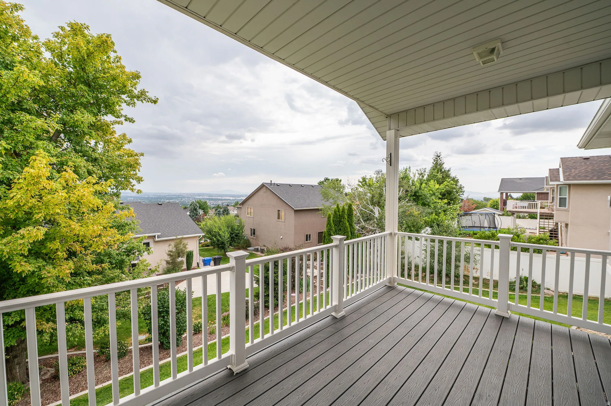 Covered deck featuring a composite wood-finish floor and white baluster railing