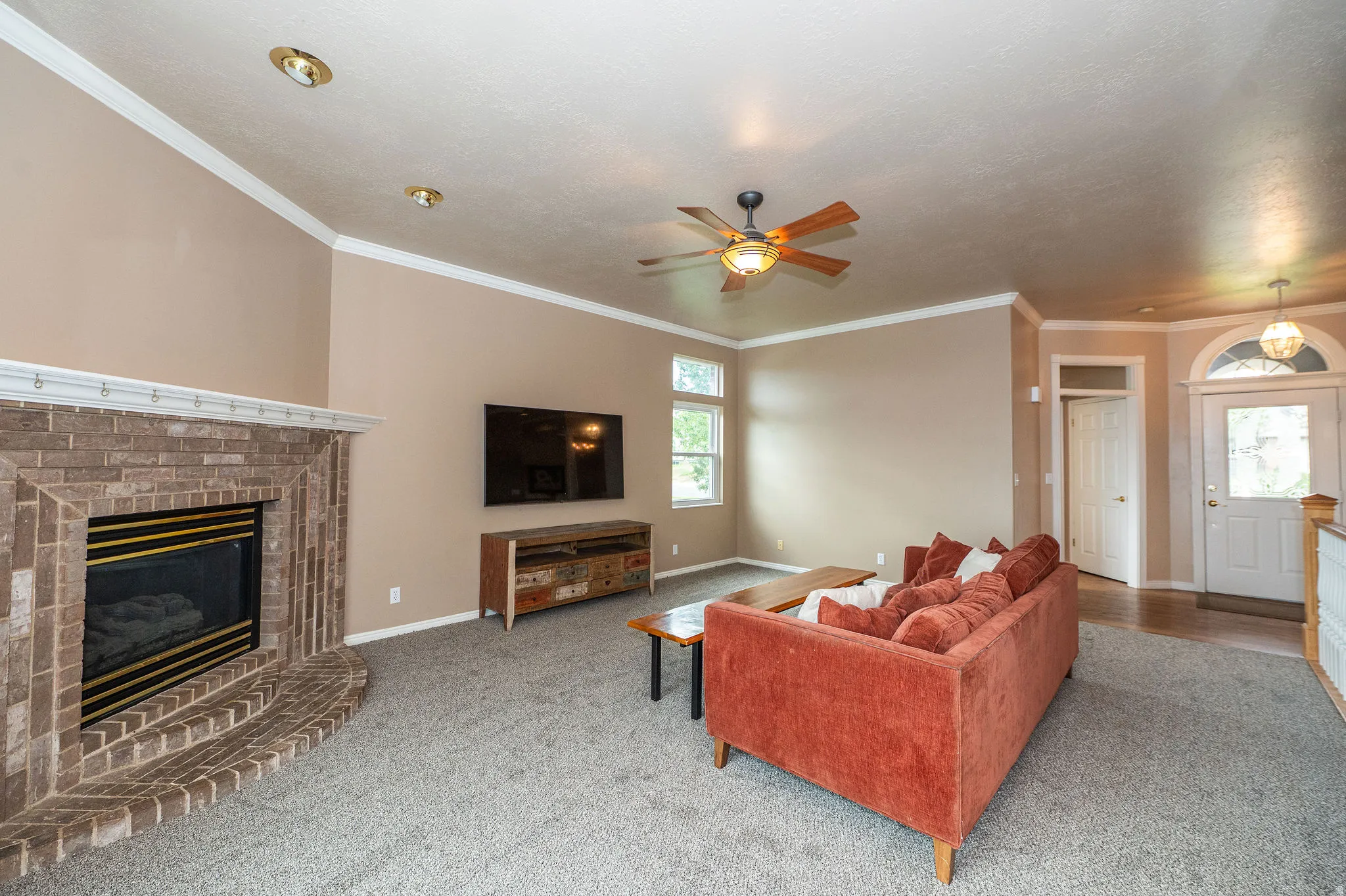 Spacious living area featuring a brick fireplace, ceiling fan, recessed lighting, and crown molding