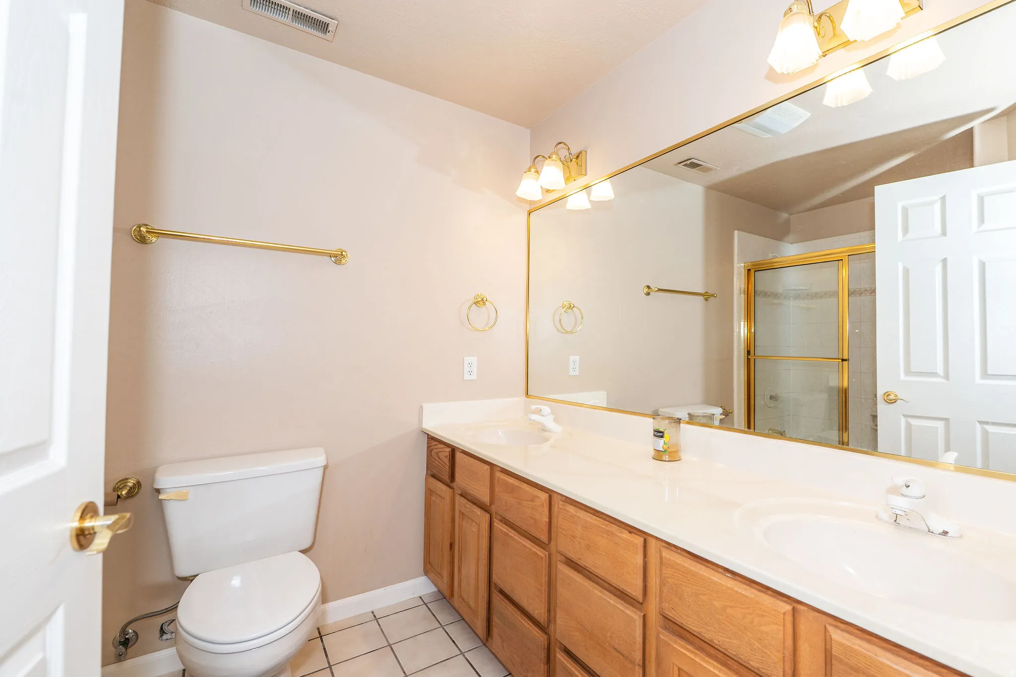 Bathroom featuring a dual sink vanity with wood cabinetry, a full-width mirror, and a toilet