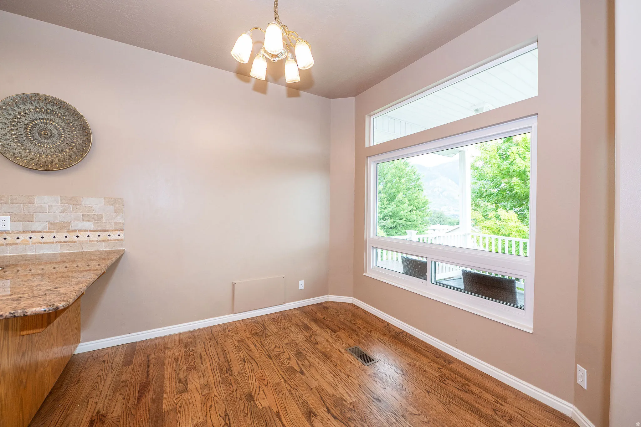 Bay window with transom above, wood-finish flooring, recessed wall, and a tile backsplash with granite countertop