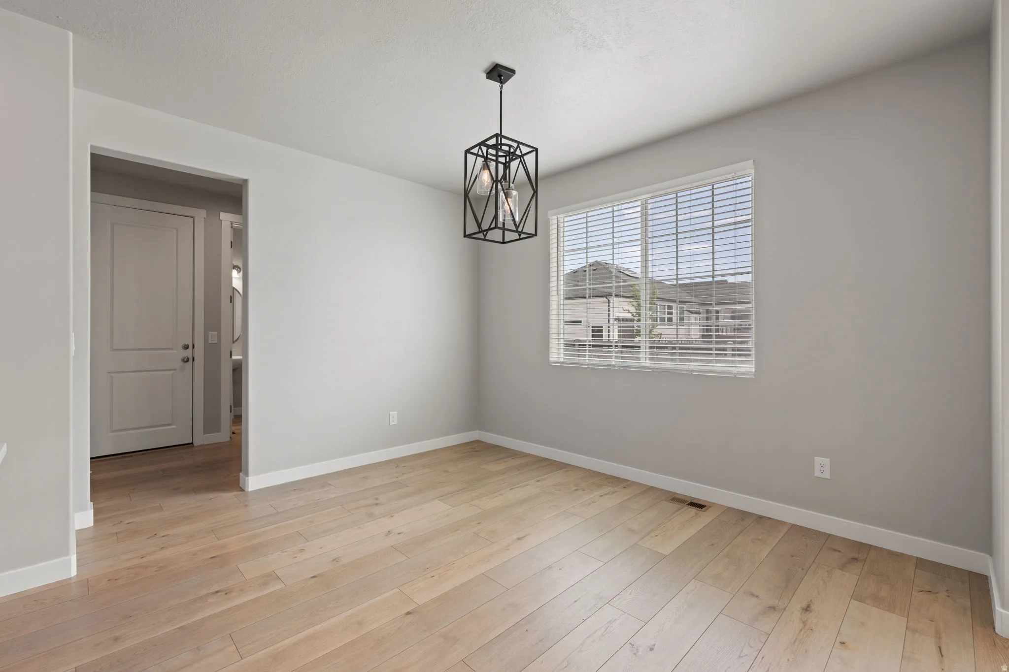Open room with light wood-finish flooring, light gray walls, and white baseboards