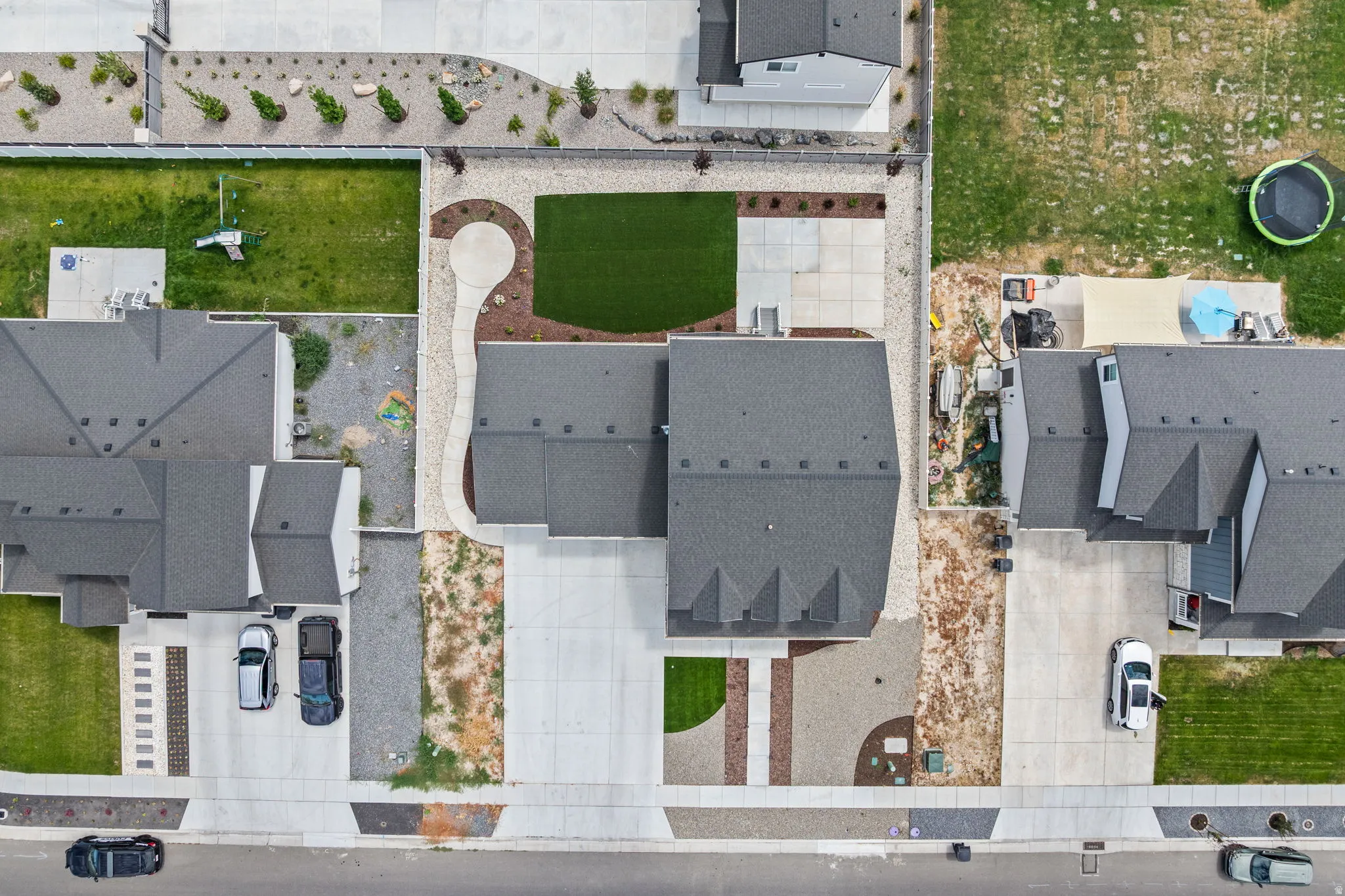 Contemporary residential property featuring a gray shingled roof, a concrete driveway, and a landscaped front yard with artificial turf
