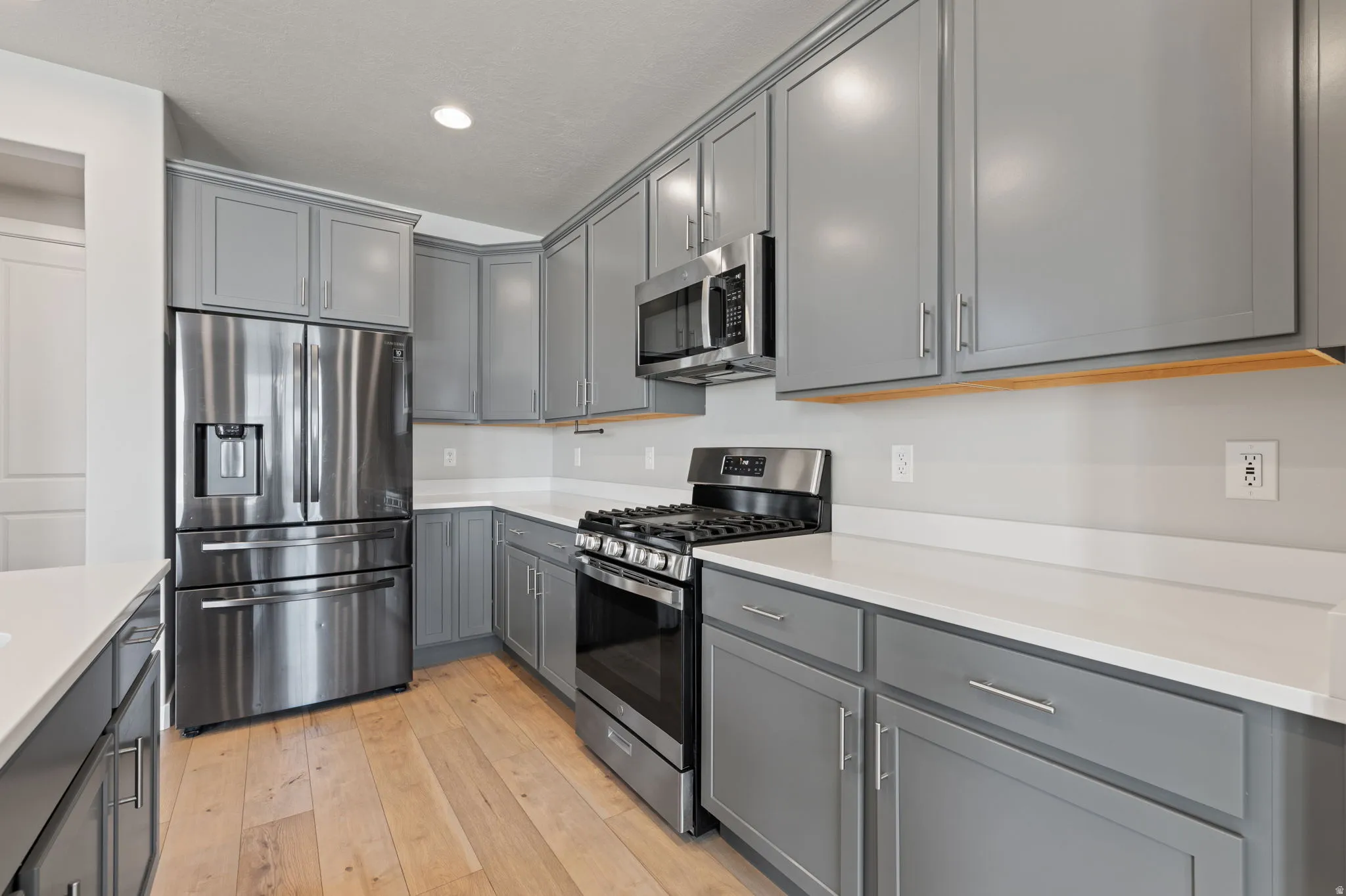 Contemporary kitchen featuring light wood-finish flooring, gray cabinetry, white countertops, and stainless steel appliances including a gas range and French door refrigerator
