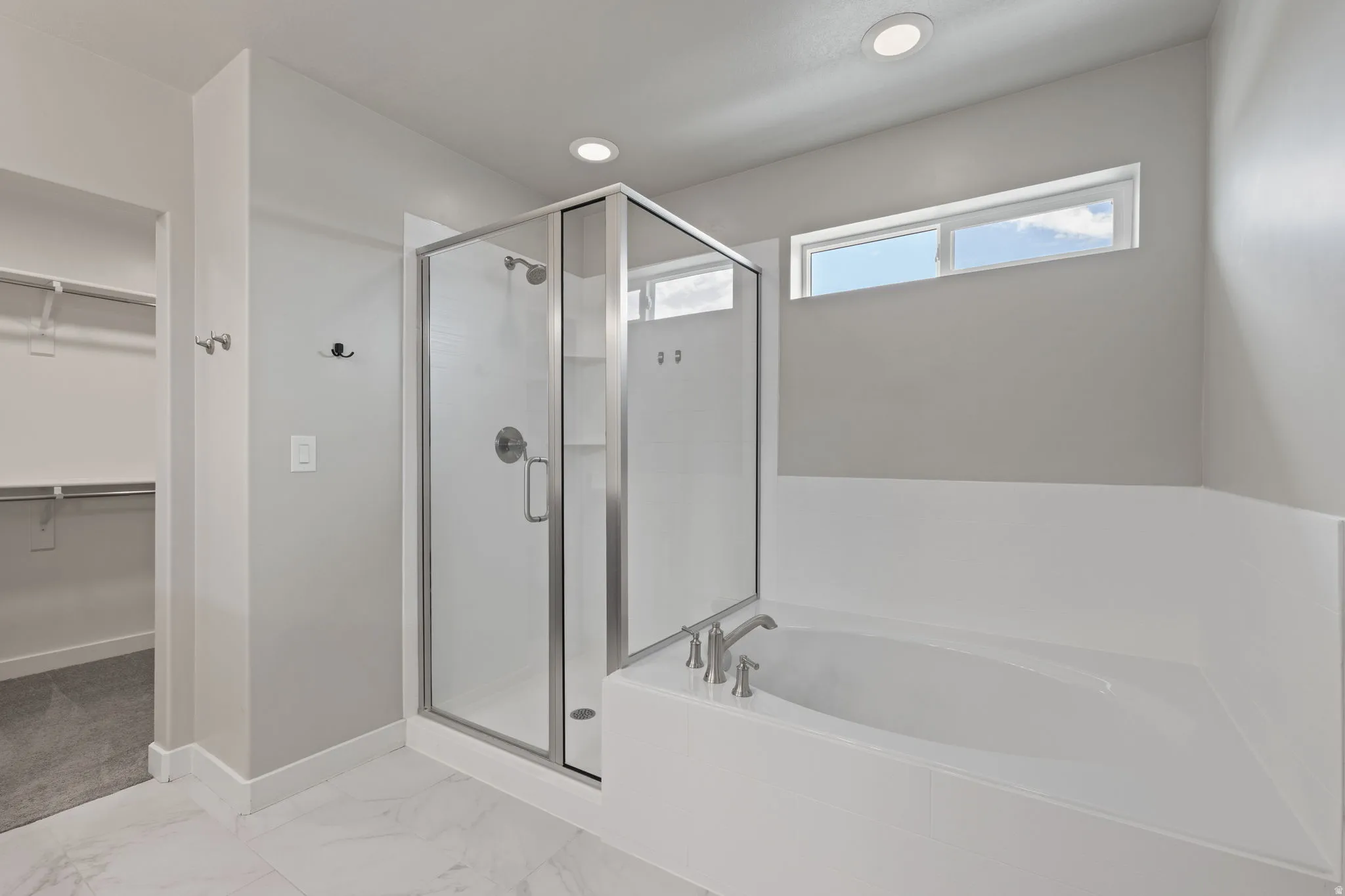 Bathroom featuring a glass-enclosed shower, built-in soaking tub with deck-mounted fixtures, marble-finish floor tiling, and a high horizontal window
