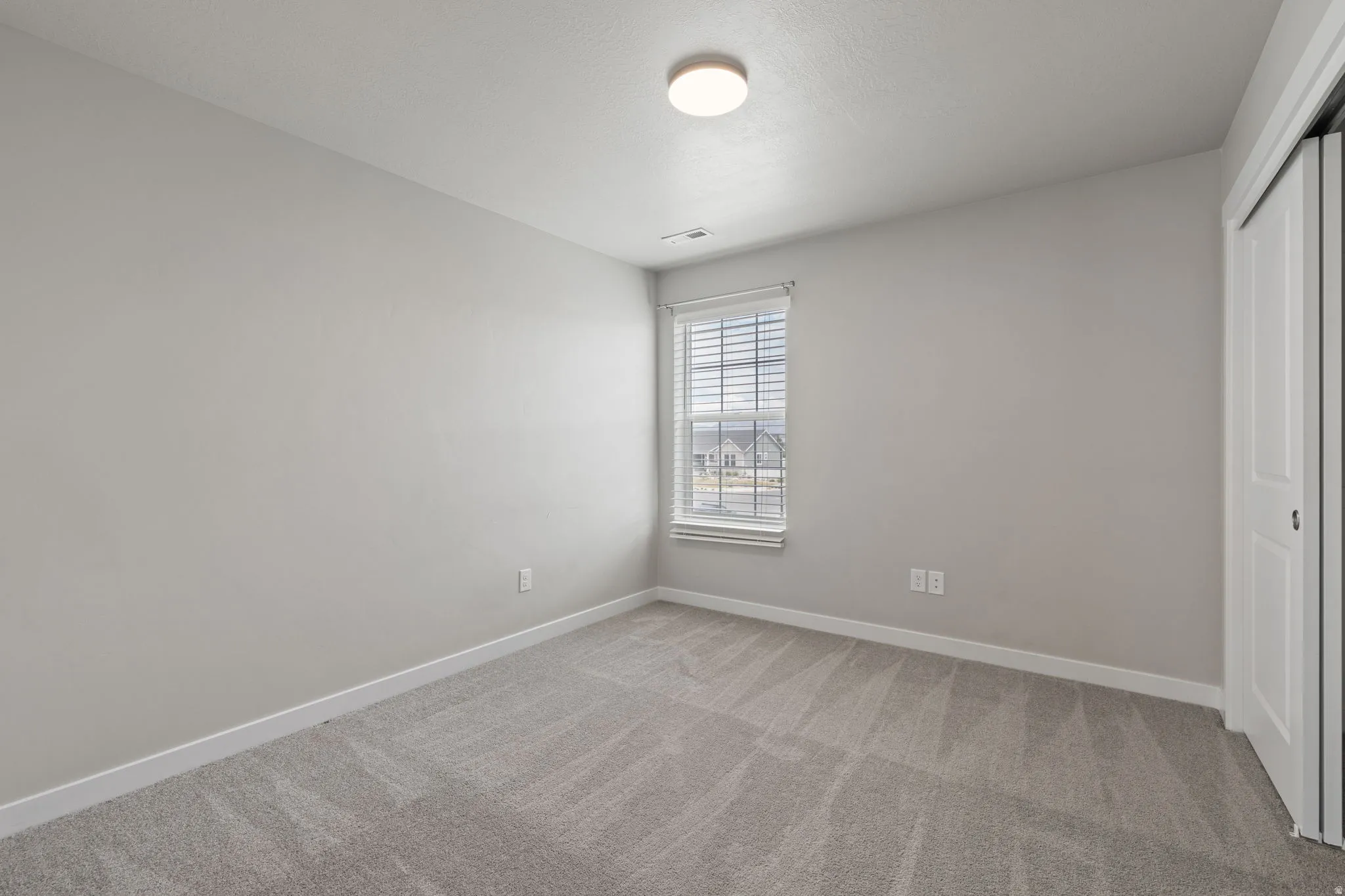 Carpeted room with a window featuring blinds, a flush mount ceiling light, and bi-fold closet doors