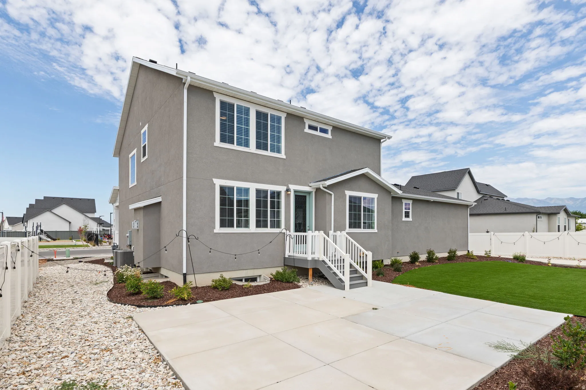 Rear exterior featuring a concrete patio, artificial turf lawn, and white privacy fencing