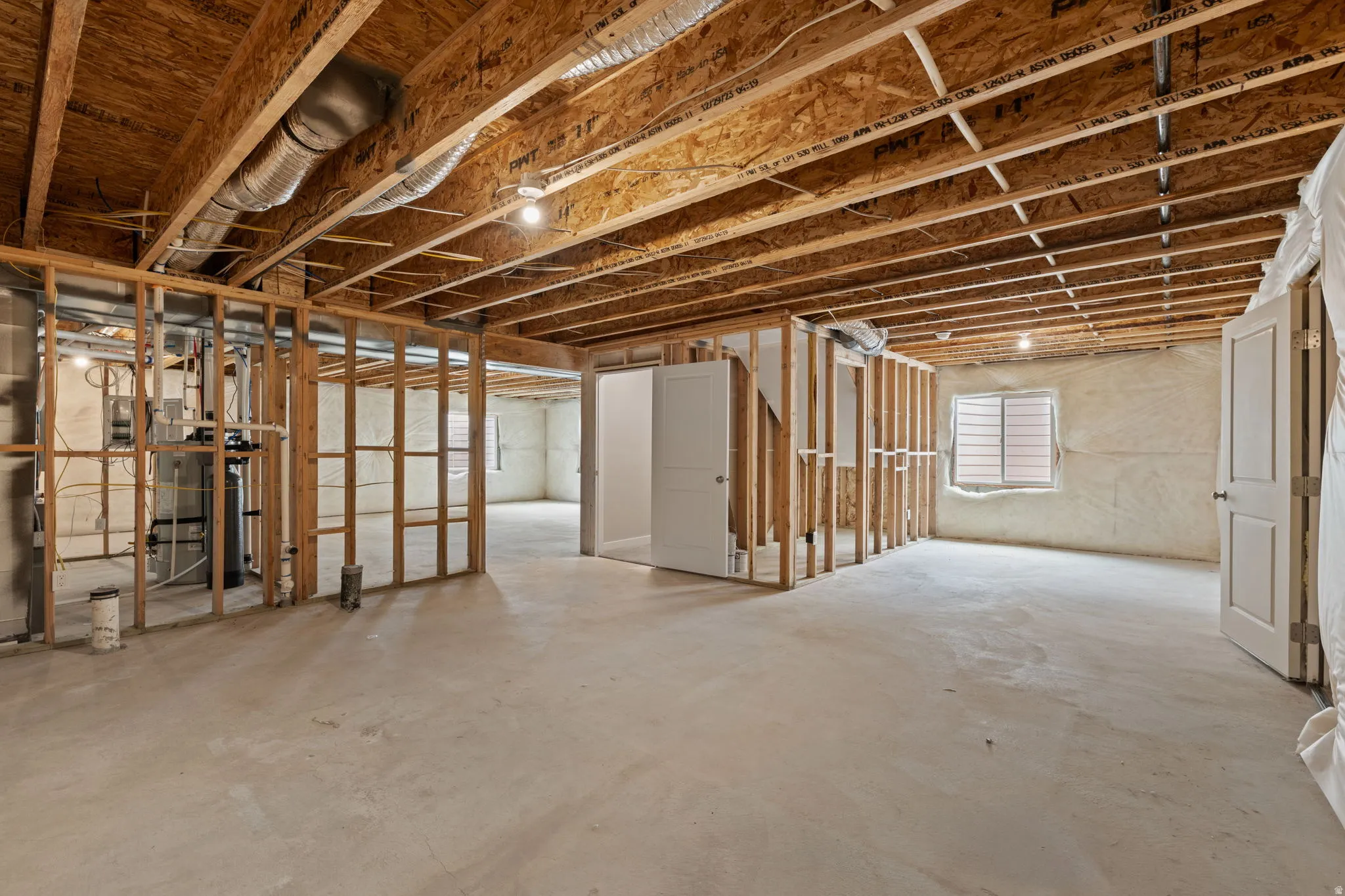 Unfinished basement featuring exposed wood joists, concrete flooring, framed wall partitions, a window with horizontal blinds, and a utility area with visible mechanical systems