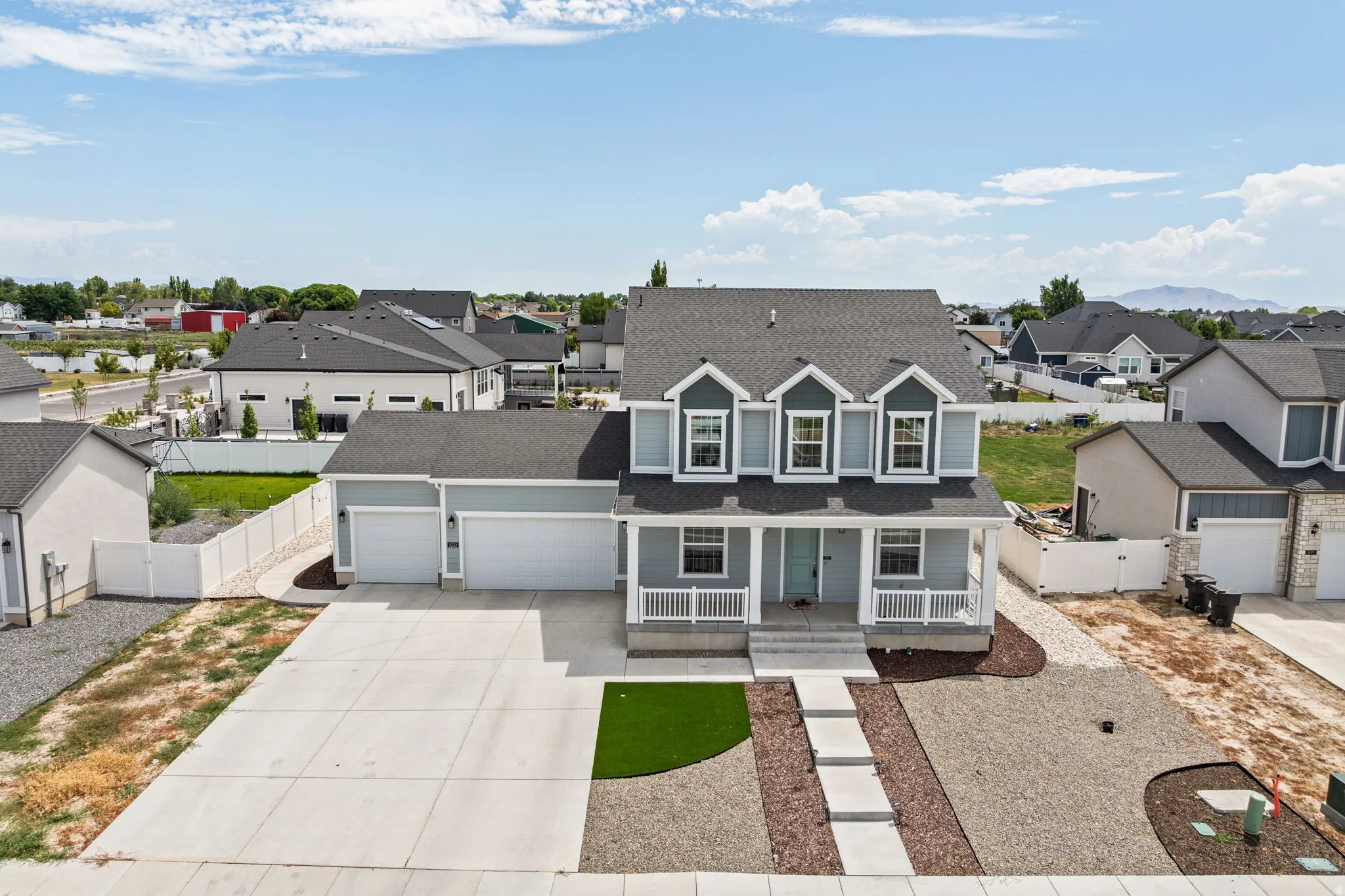Contemporary two-story home featuring a three-car garage, a covered front porch with white railings, and a light blue exterior with dark gray accents