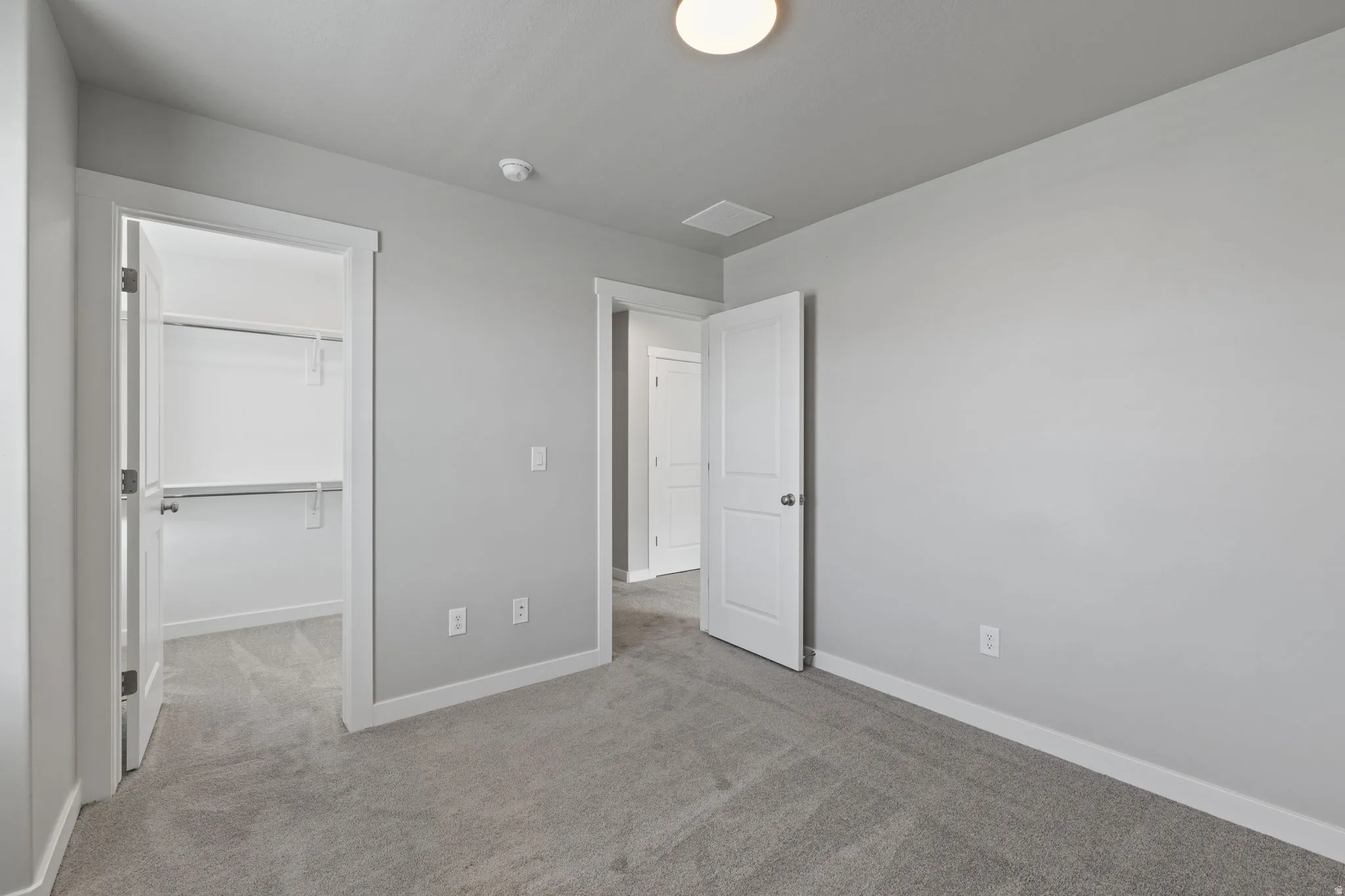 Spacious room featuring light gray wall paint, plush gray carpeting, white trim, and a white two-panel interior door