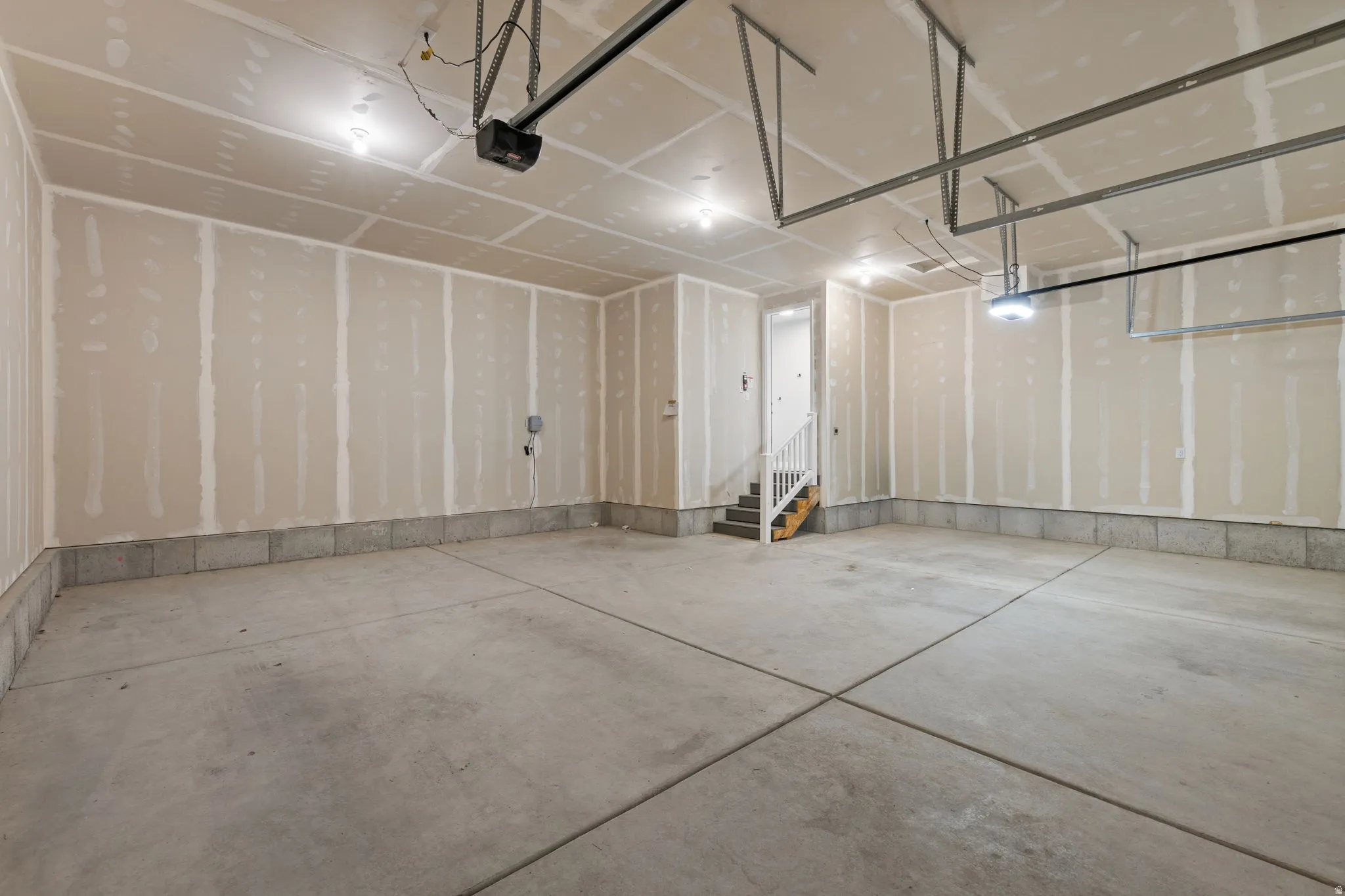 Spacious garage featuring a concrete floor, overhead lighting, garage door opener, and interior stairs with a white railing