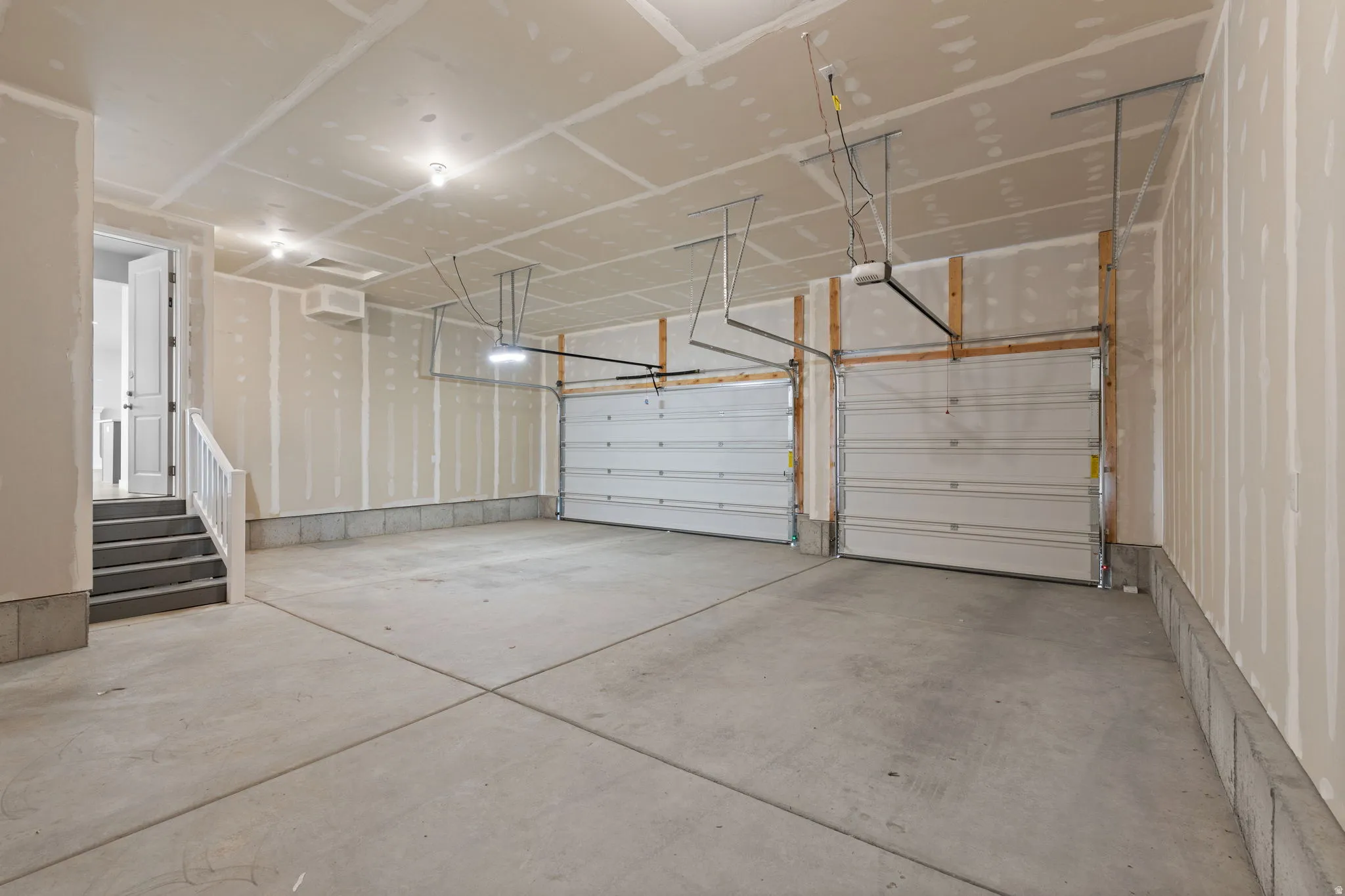 Spacious two-car garage featuring a concrete floor, two individual garage doors with openers, exposed drywall, and overhead lighting