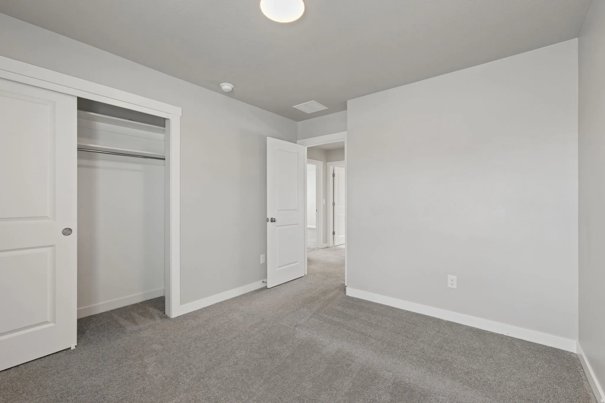 Bedroom featuring light gray walls, gray carpet, white trim, and a double-sliding closet with integrated shelving and hanging rod
