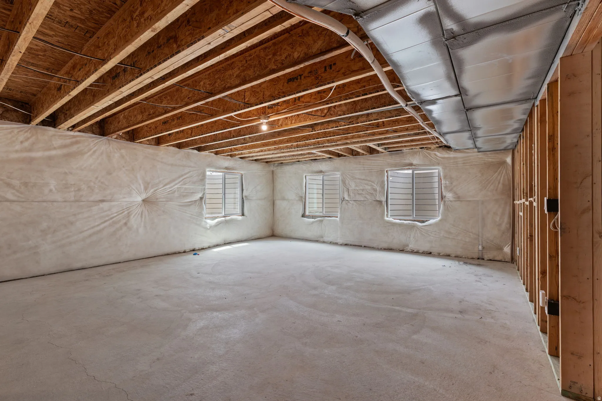 Unfinished basement with exposed wood joists and subfloor, concrete flooring, and multiple egress windows
