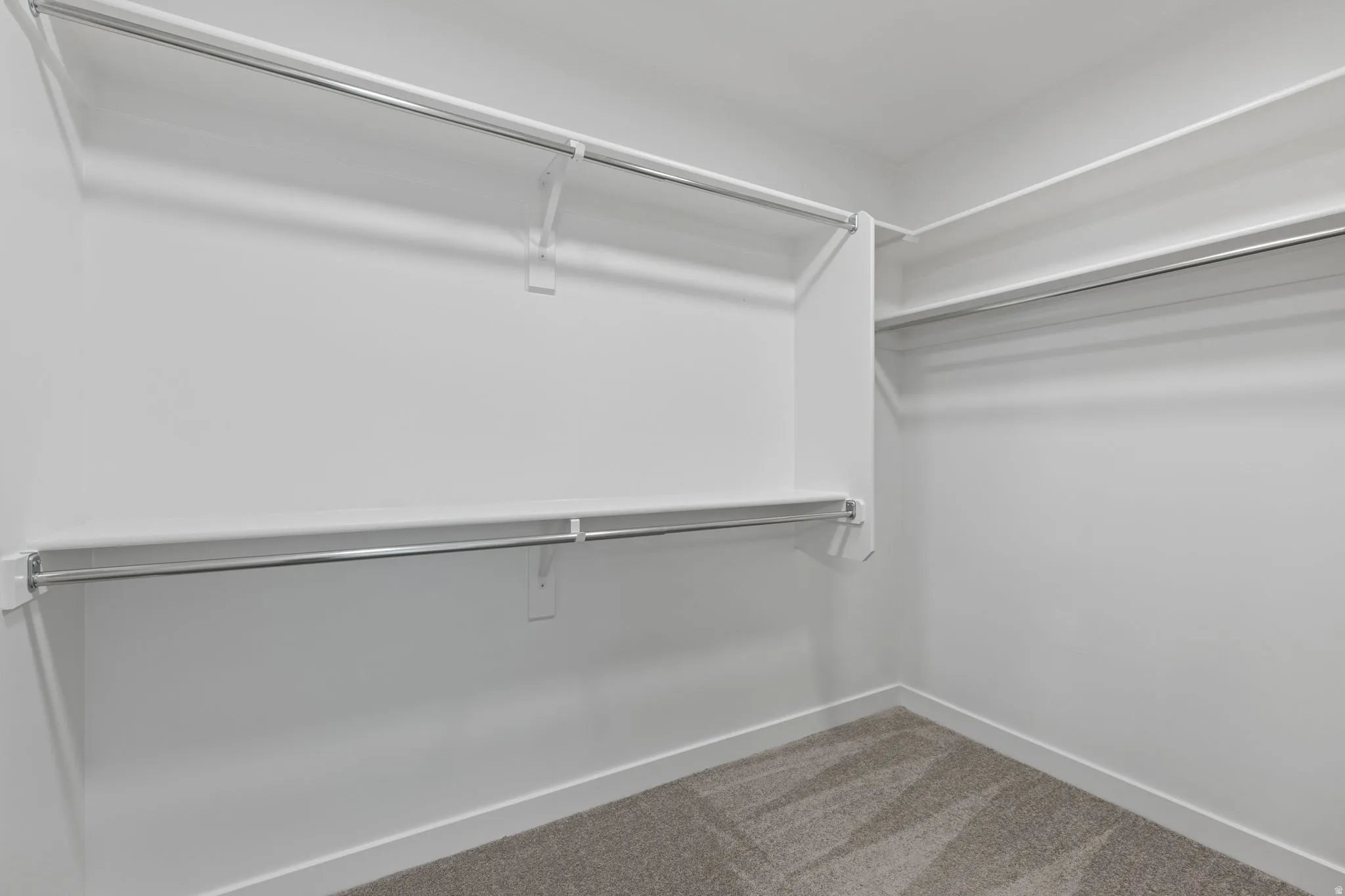 Walk-in closet featuring white painted walls, white shelving, and chrome hanging rods