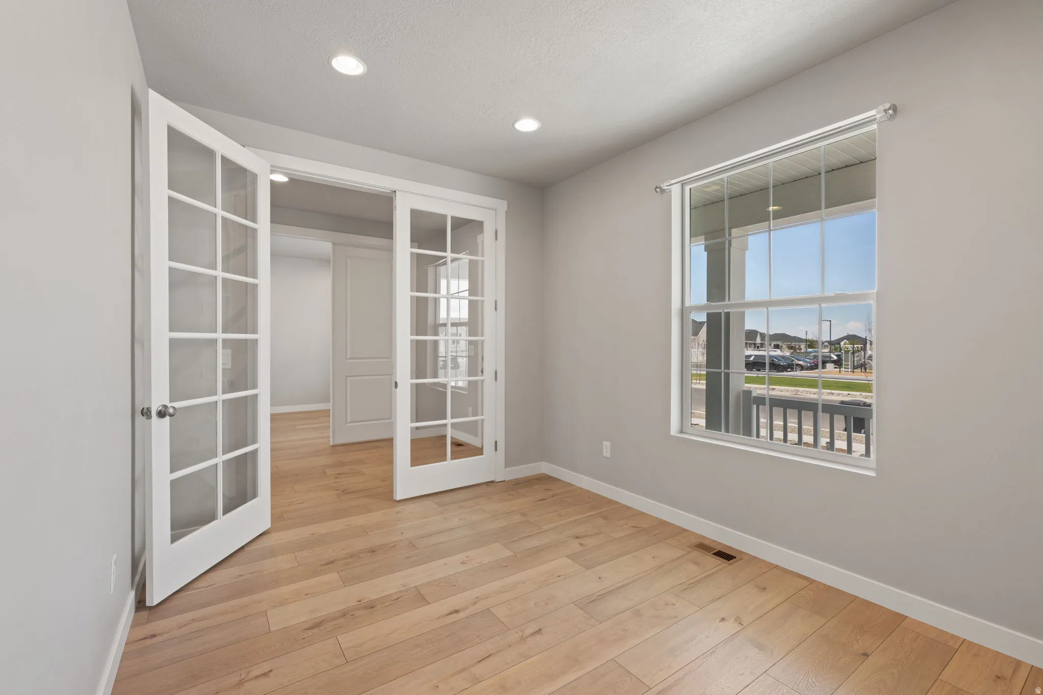 Room featuring French doors with glass panes, wood-finish flooring, recessed lighting, and a large window with white trim