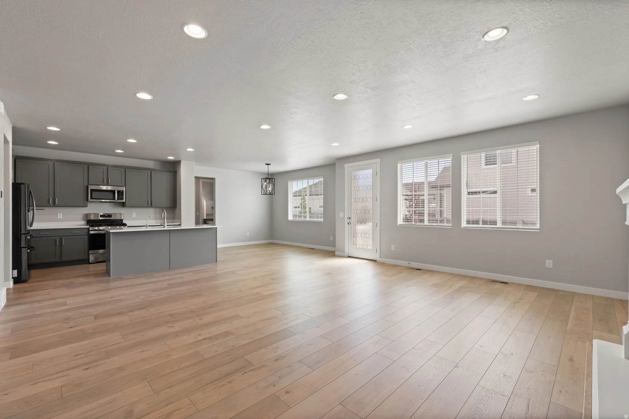 Open-concept living area featuring wood-finish flooring, recessed lighting, and a kitchen with gray cabinetry and stainless steel appliances