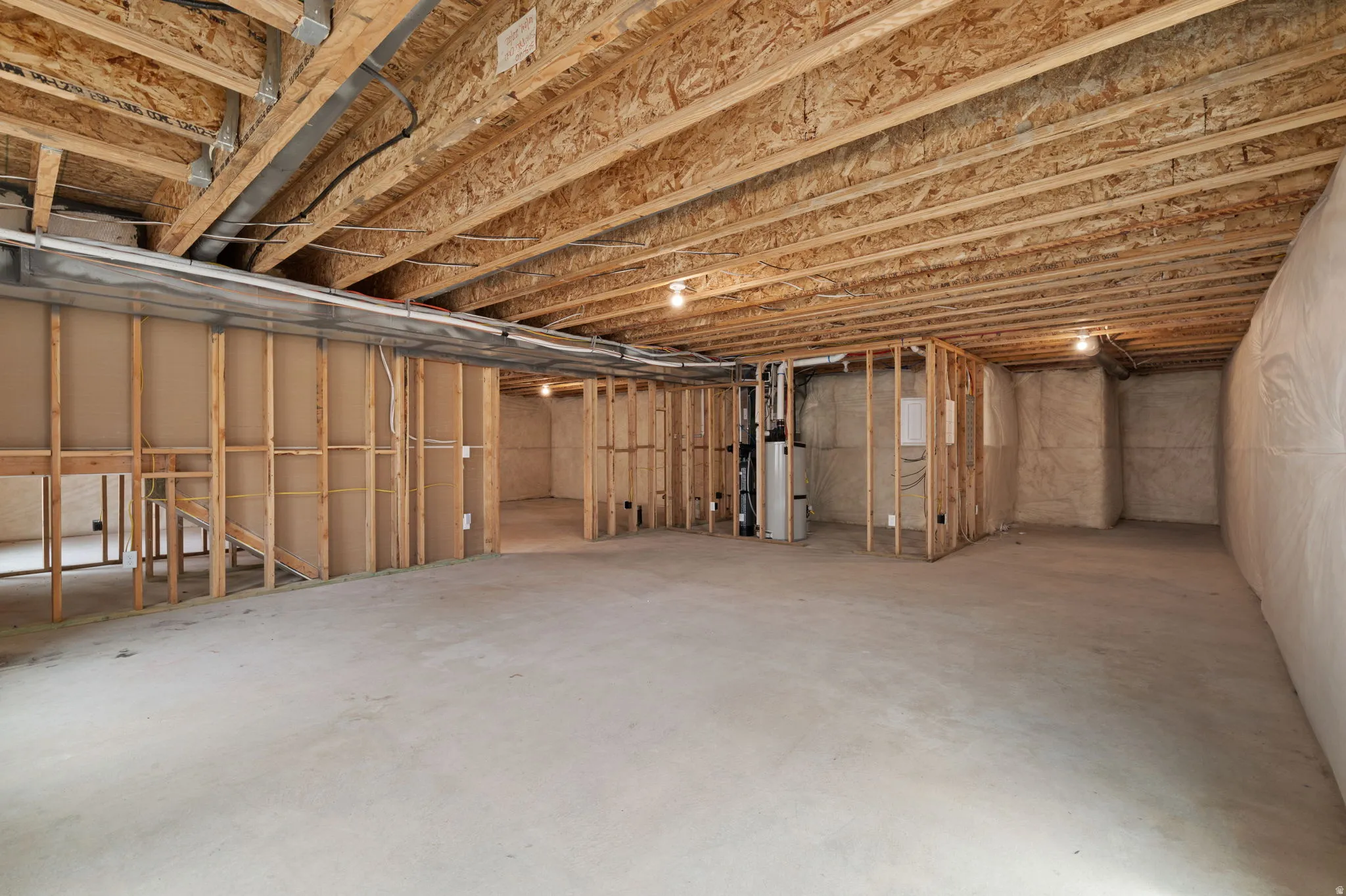 Unfinished basement featuring exposed wood joists and subflooring, concrete slab, framed interior walls, and a visible water heater
