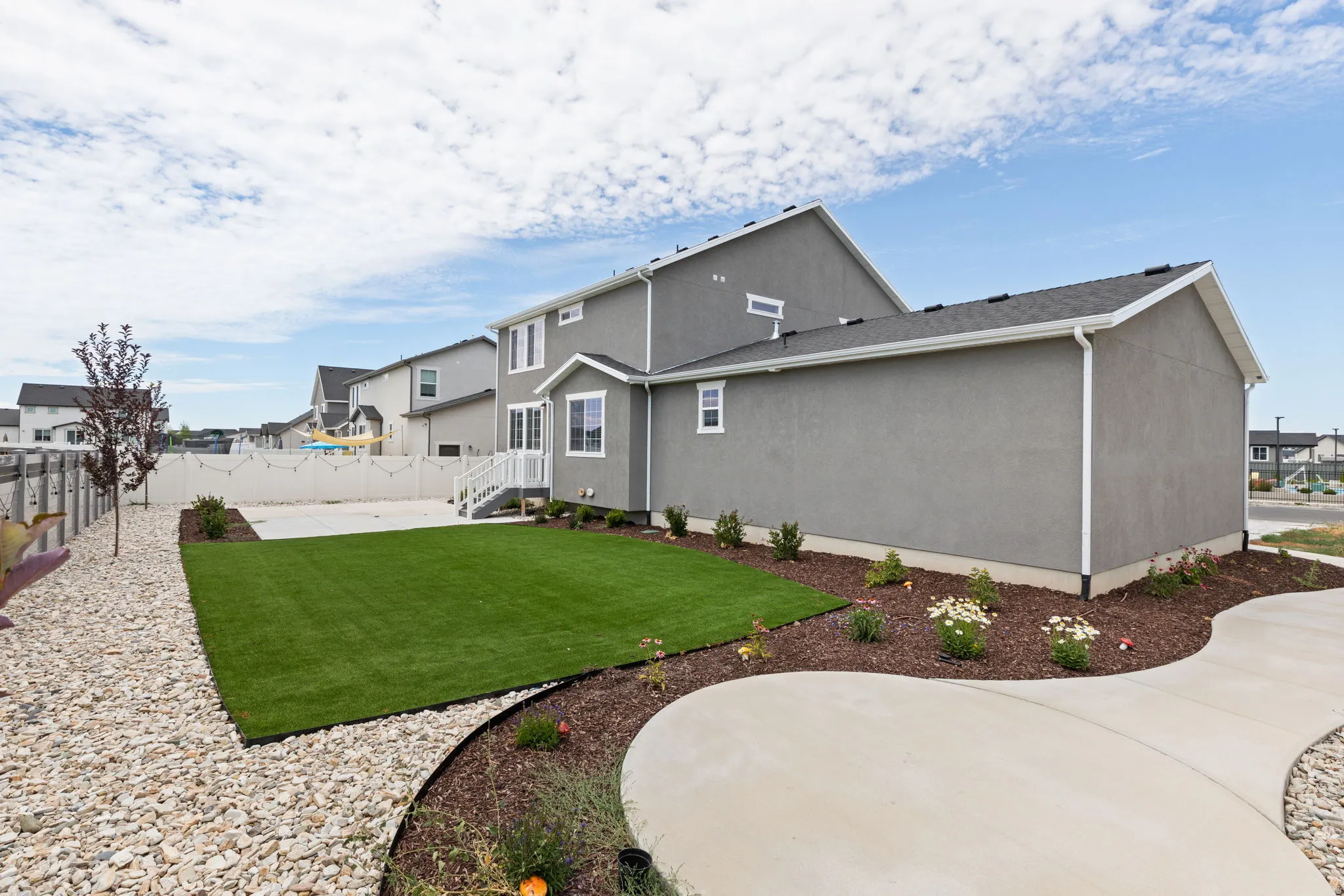 Expansive backyard featuring a manicured lawn, concrete patio, and decorative rock landscaping