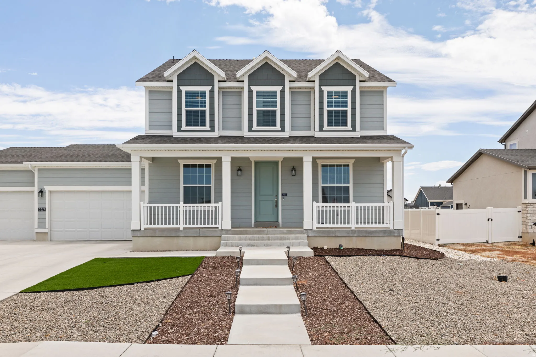 Two-story residence featuring light gray siding with dark gray gables, a covered front porch with white railings, and a light-colored front door