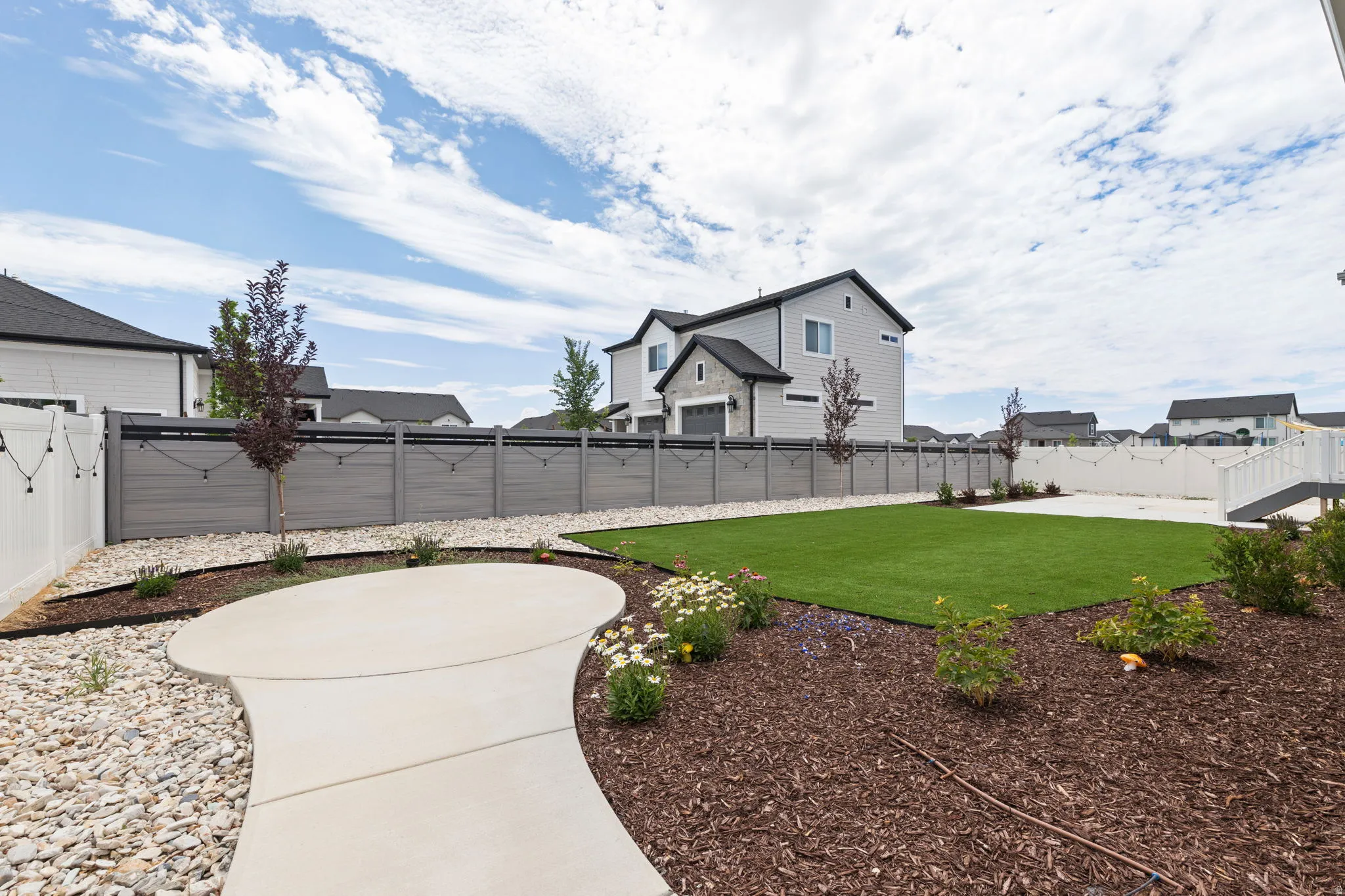 Spacious backyard featuring an artificial turf lawn, a curved concrete patio, and a decorative rock area