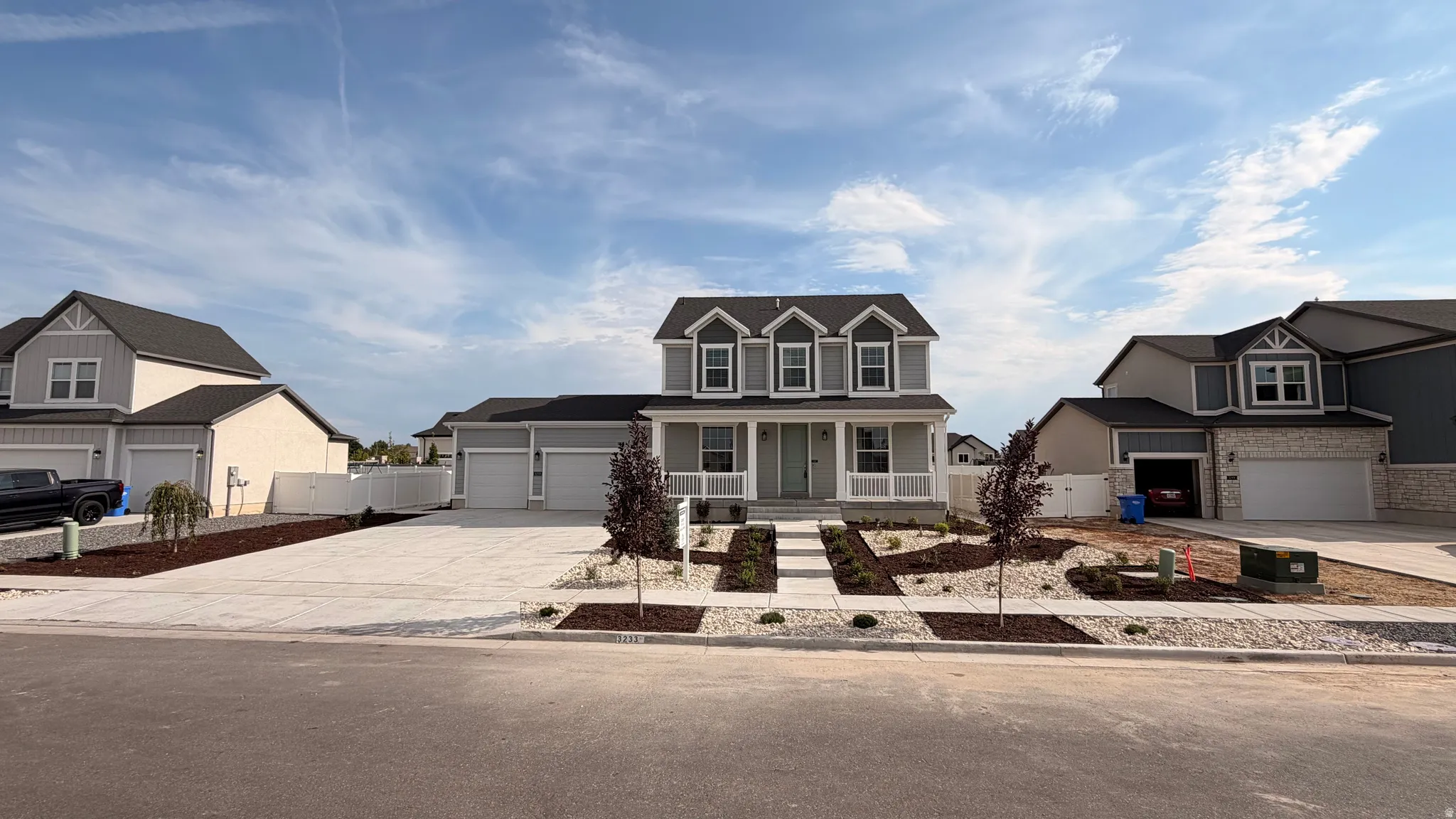 Two-story Colonial with four-panel garage doors, covered front porch with decorative columns, and manicured front landscaping including newly planted shrubs and stone hardscaping