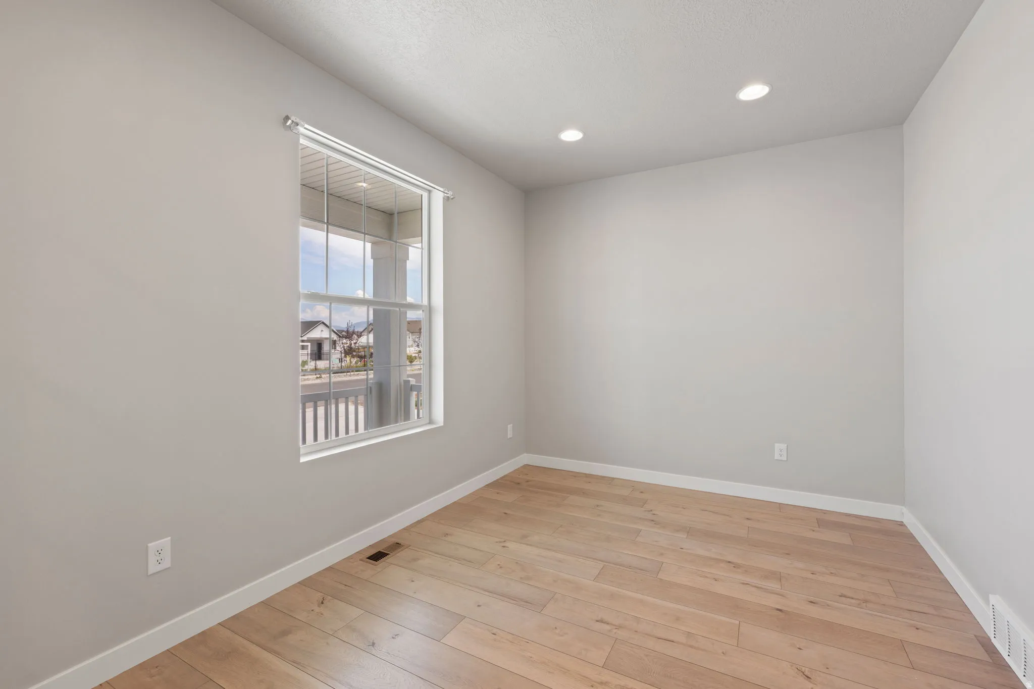 Light-filled room featuring wood-finish flooring, recessed lighting, a double-hung window, and neutral wall tones