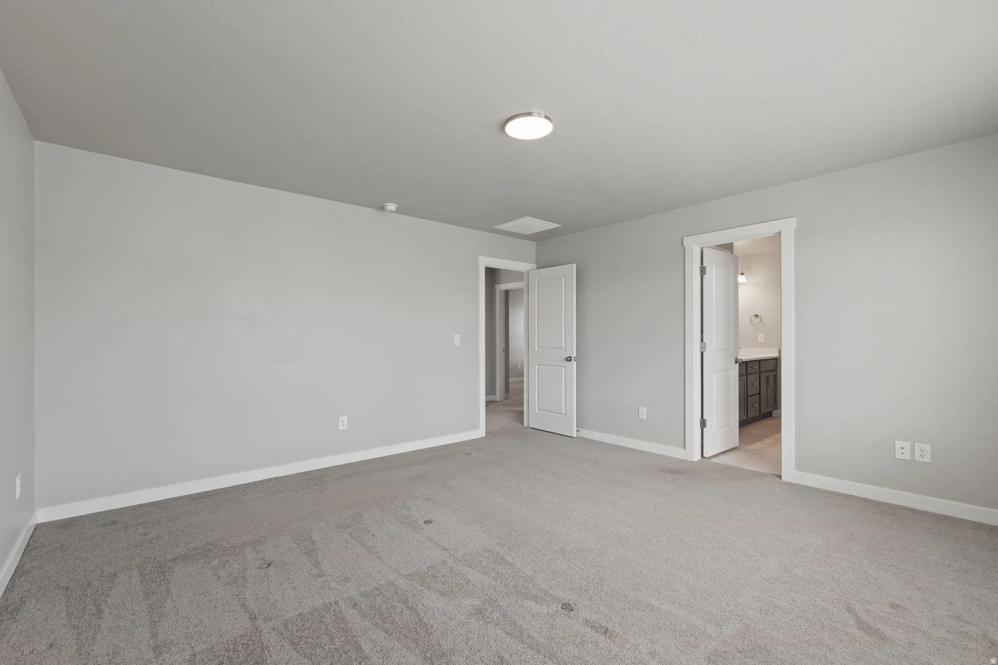Spacious room featuring light gray carpeting, neutral wall paint, white trim, a flush-mount ceiling light, and access to a bathroom with a vanity