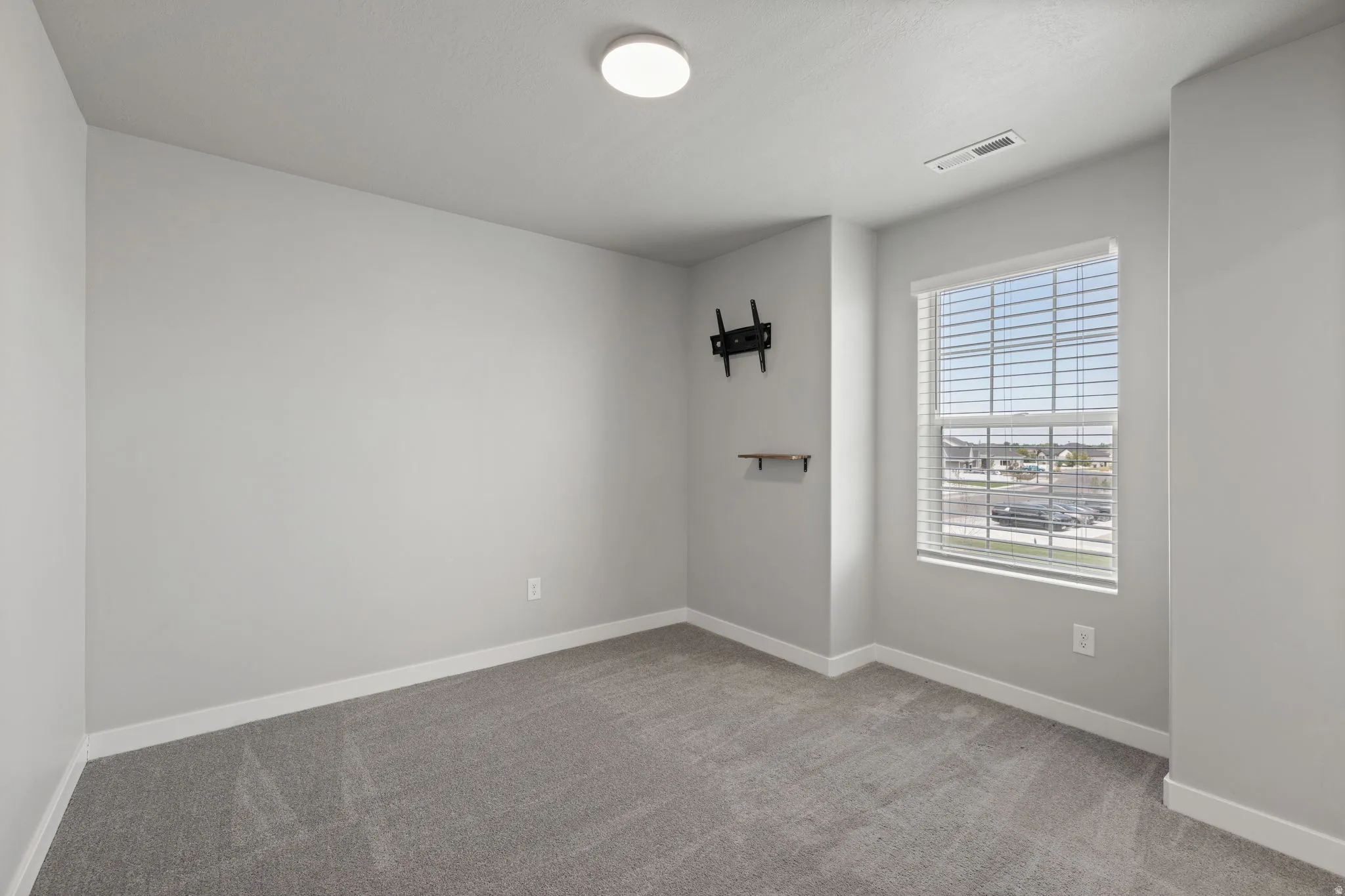 Interior room featuring gray textured carpeting, light gray wall paint, and white baseboards