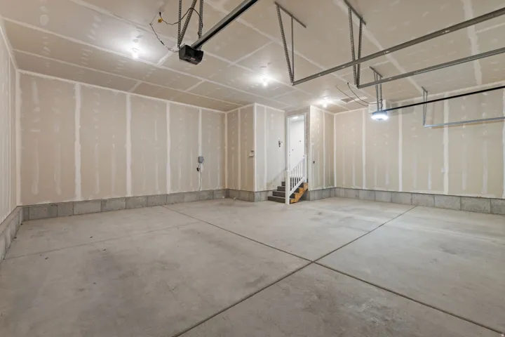 Spacious garage featuring a concrete floor, overhead lighting, garage door opener, and interior stairs with a white railing