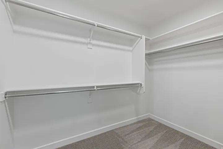 Walk-in closet featuring white painted walls, white shelving, and chrome hanging rods