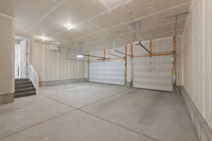 Spacious two-car garage featuring a concrete floor, two individual garage doors with openers, exposed drywall, and overhead lighting
