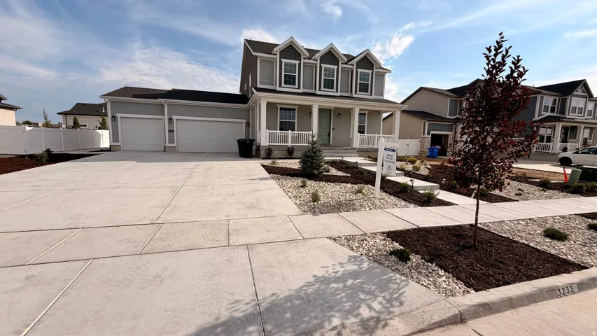 Elegant two-story Colonial featuring a spacious concrete driveway with multiple parking spaces, manicured front landscaping with newly planted trees and mulched beds, and a three-car garage