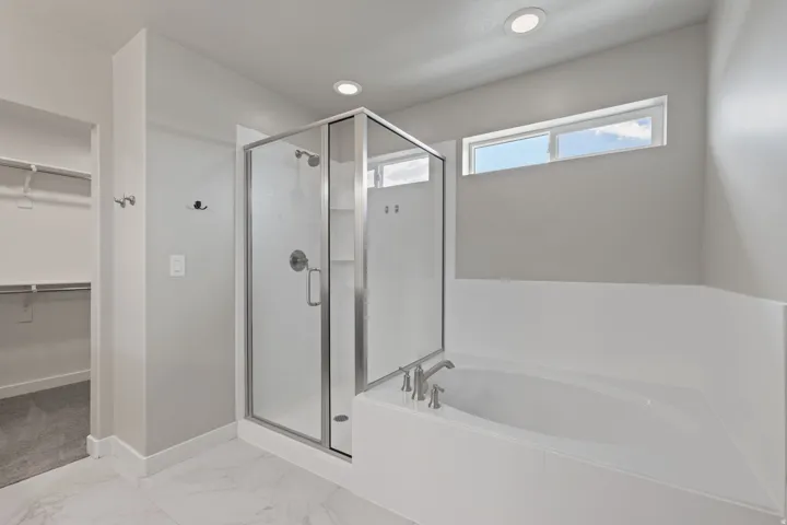 Bathroom featuring a glass-enclosed shower, built-in soaking tub with deck-mounted fixtures, marble-finish floor tiling, and a high horizontal window