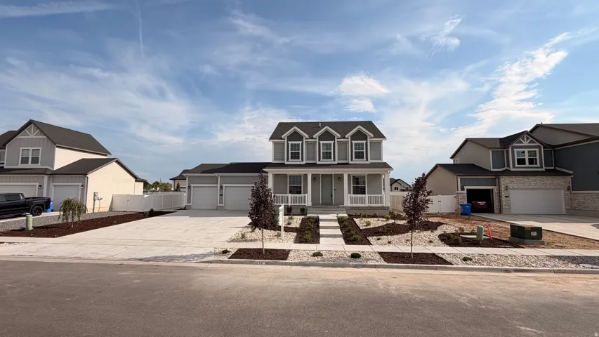 Two-story Colonial with four-panel garage doors, covered front porch with decorative columns, and manicured front landscaping including newly planted shrubs and stone hardscaping